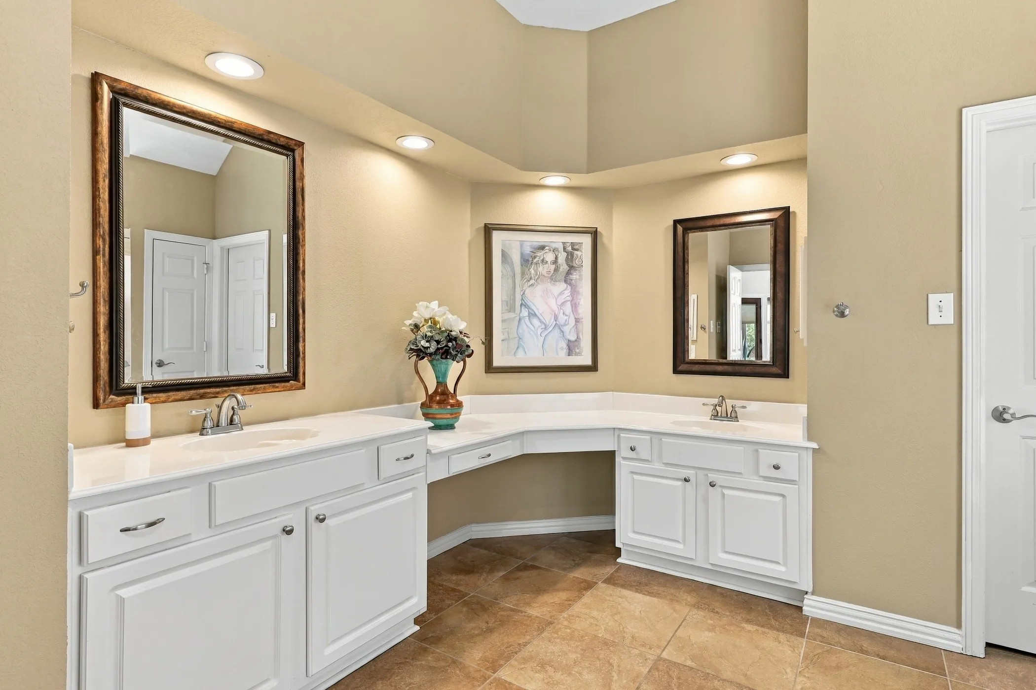 Spacious vanity area featuring dual sinks, white cabinetry, integrated lighting, and tile flooring