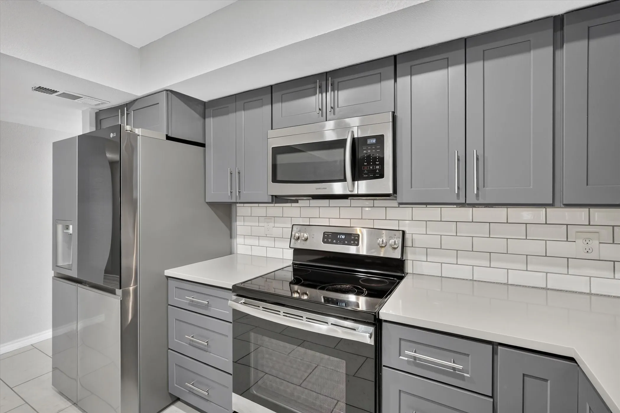 Kitchen featuring blueish gray cabinetry, stainless steel appliances, white subway tile backsplash, and light-toned tile flooring