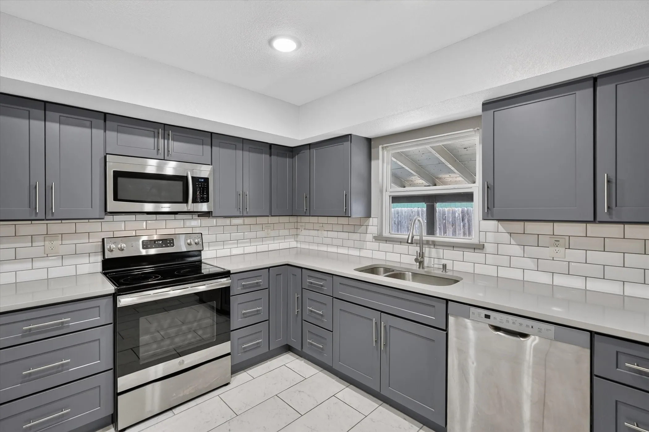 Kitchen featuring blueish gray cabinetry, stainless steel appliances, white subway tile backsplash, and light-toned tile flooring