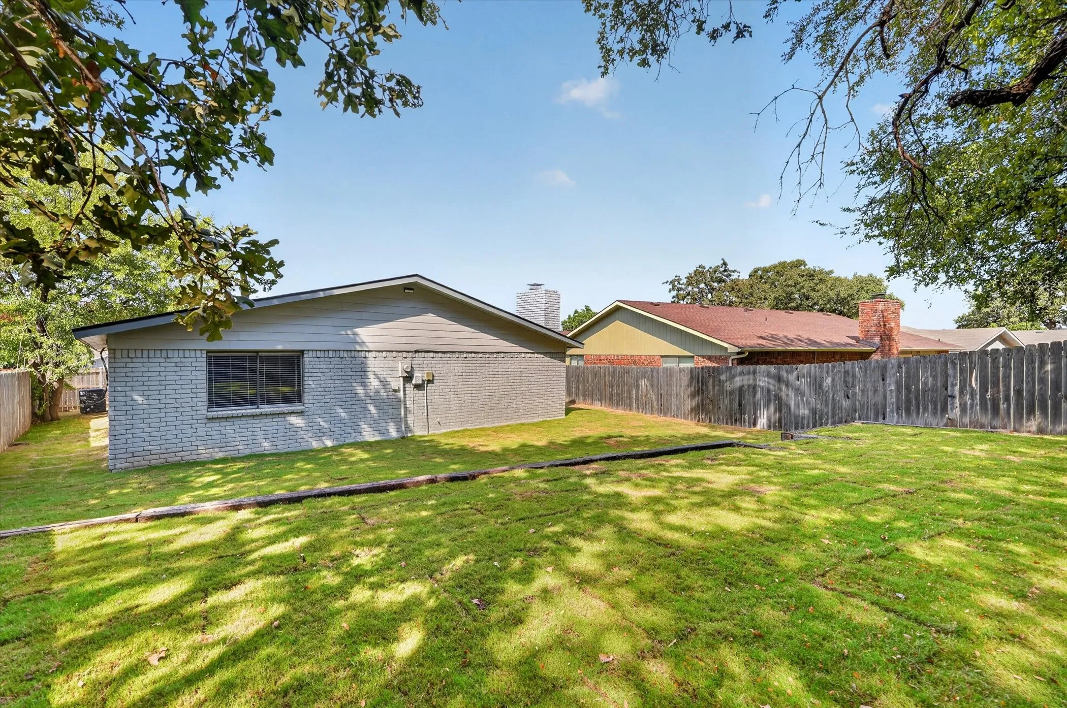 Expansive grassy area with mature trees providing partial shade, featuring a privacy fence
