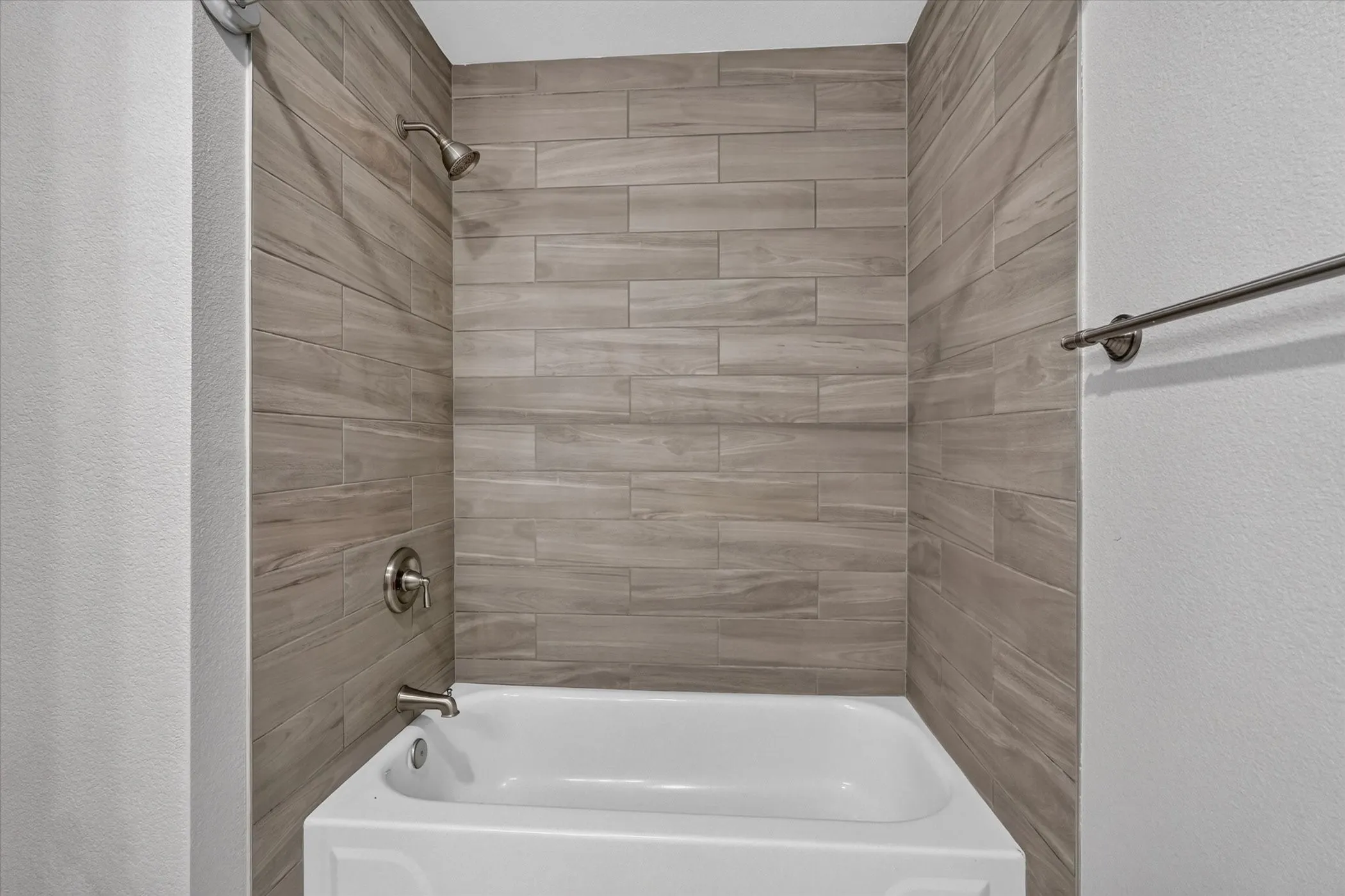 Hallway bathtub with wood-finish tile surround, brushed nickel showerhead, and tasteful finishes