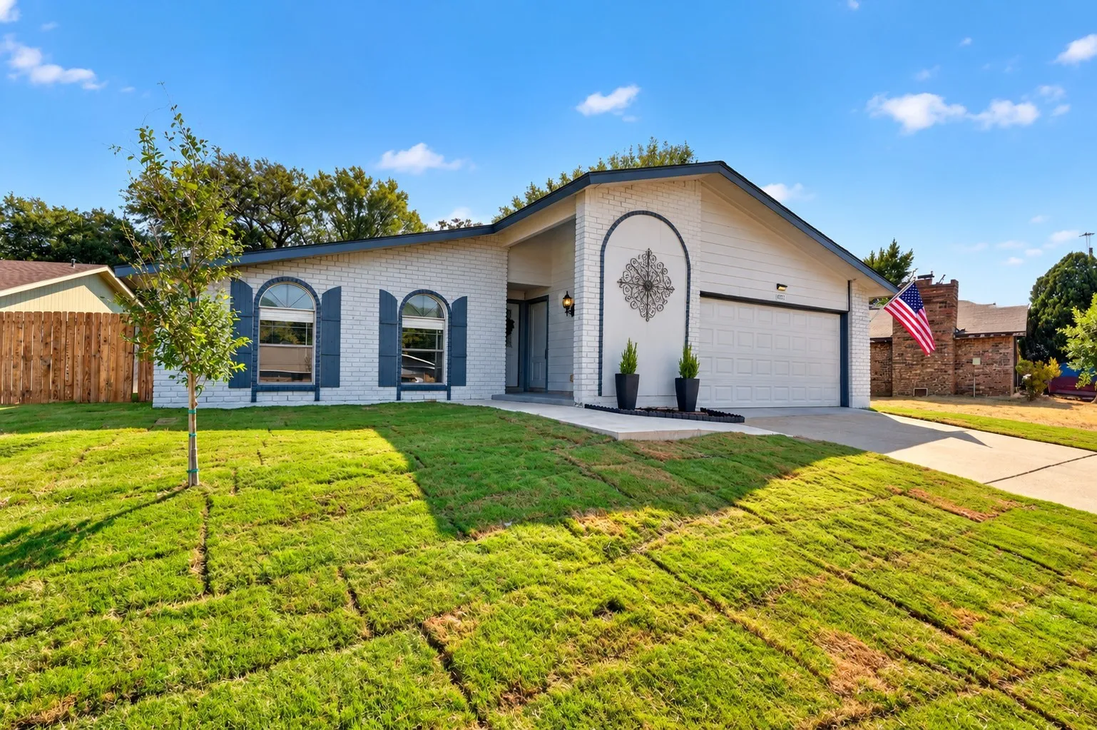 brick exterior with contrasting dark trim, attached garage, arched windows with decorative shutters with new sod