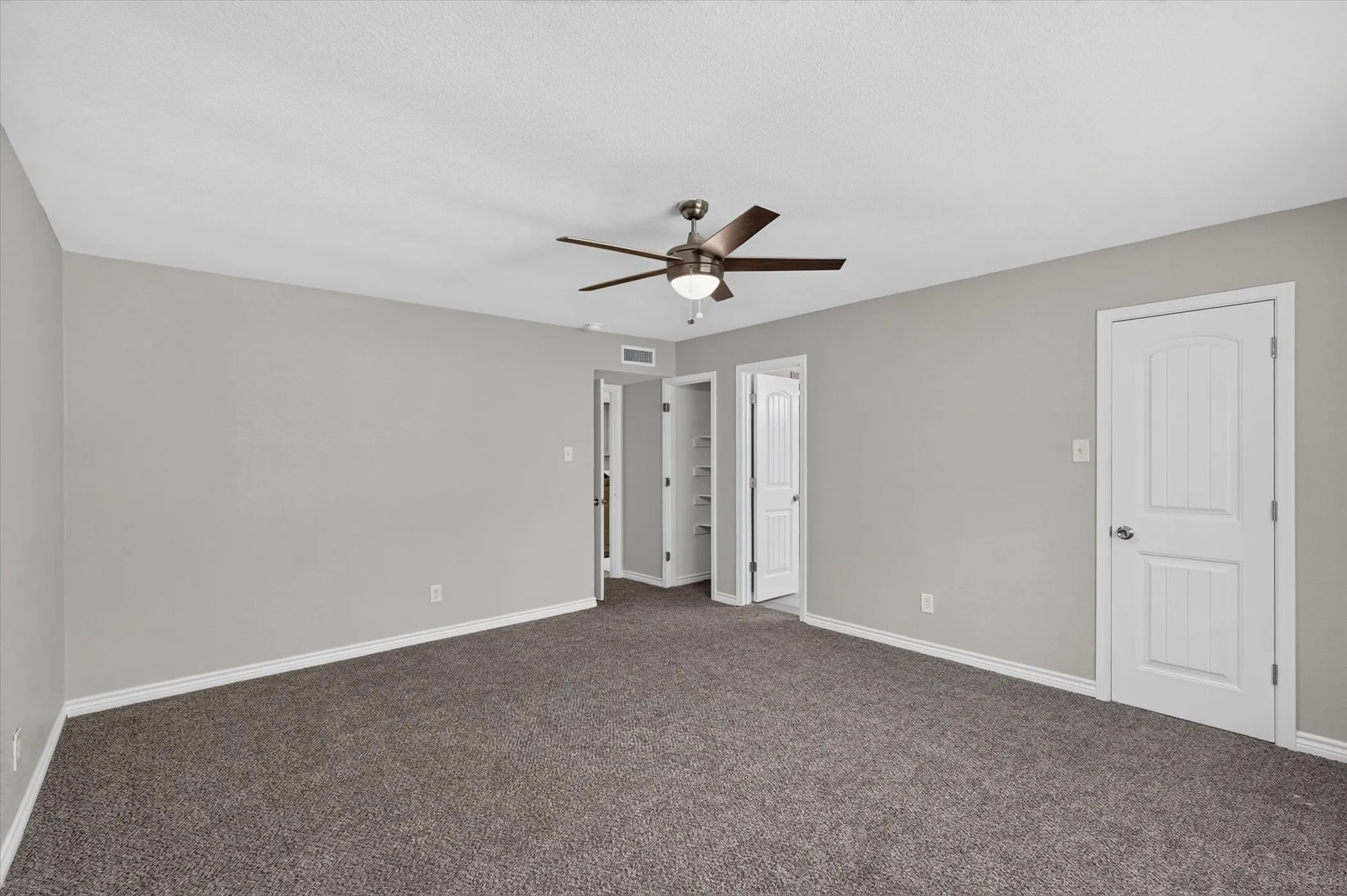Large primary bedroom with Neutral wall paint, ceiling fan, carpet flooring, window with blinds, and white trim