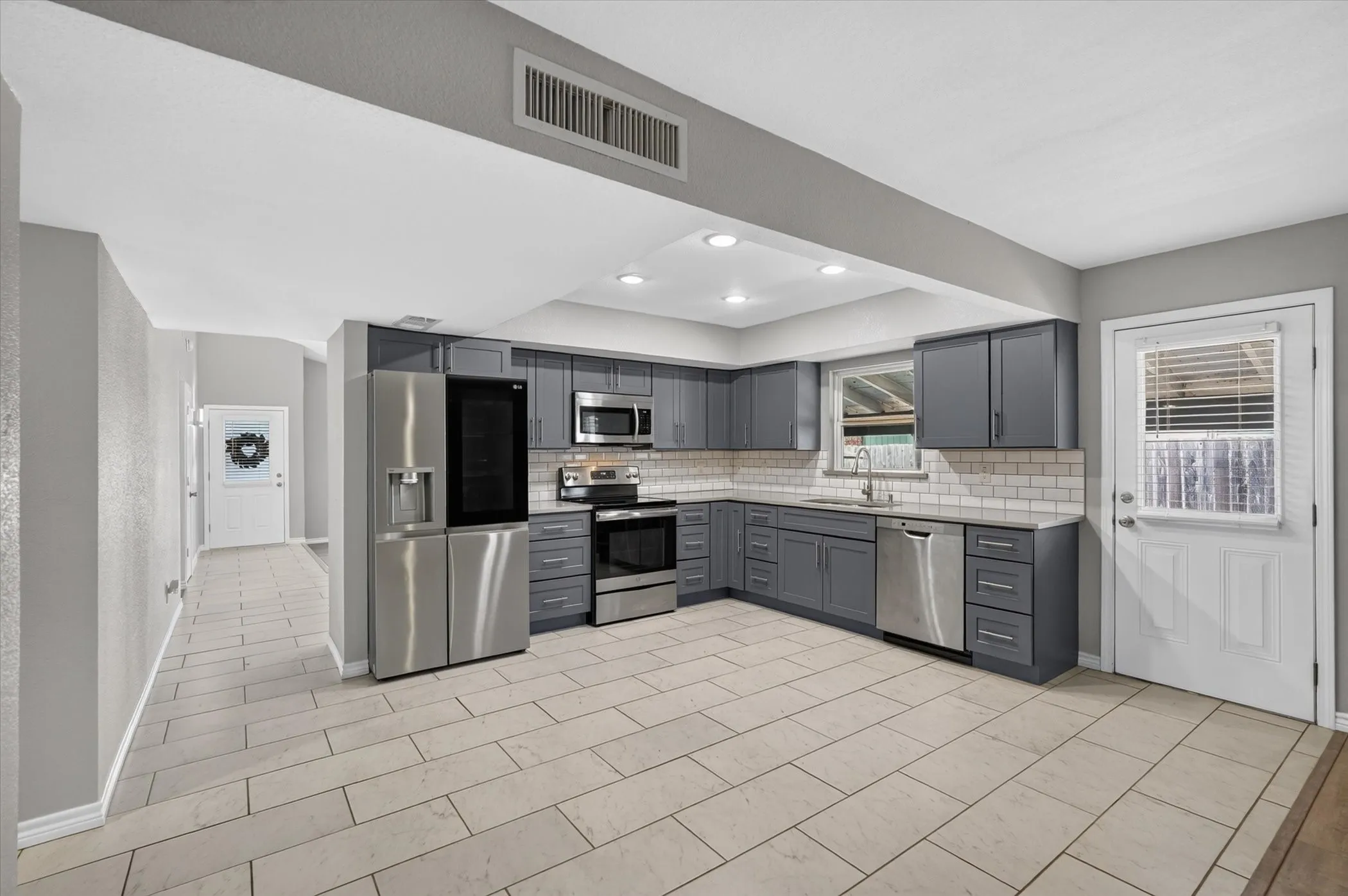 Kitchen featuring blueish gray cabinetry, stainless steel appliances, white subway tile backsplash, and light-toned tile flooring