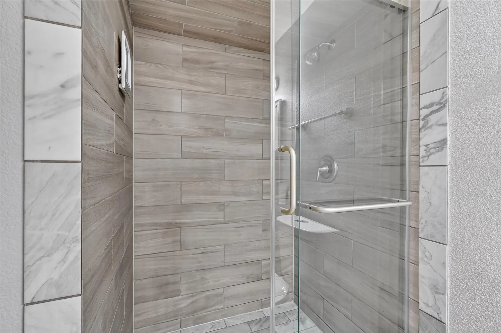 Enclosed shower with clear glass door, wood-finish tile walls, and a tiled shower floor