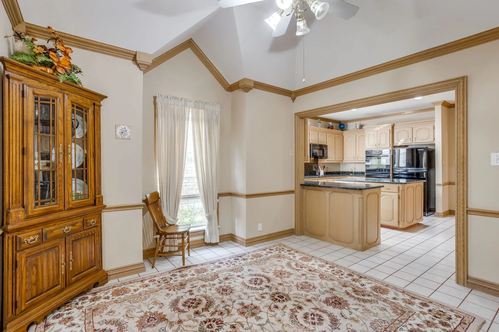 Vaulted ceiling with a ceiling fan, white tile flooring, and an arched entryway leading to the kitchen