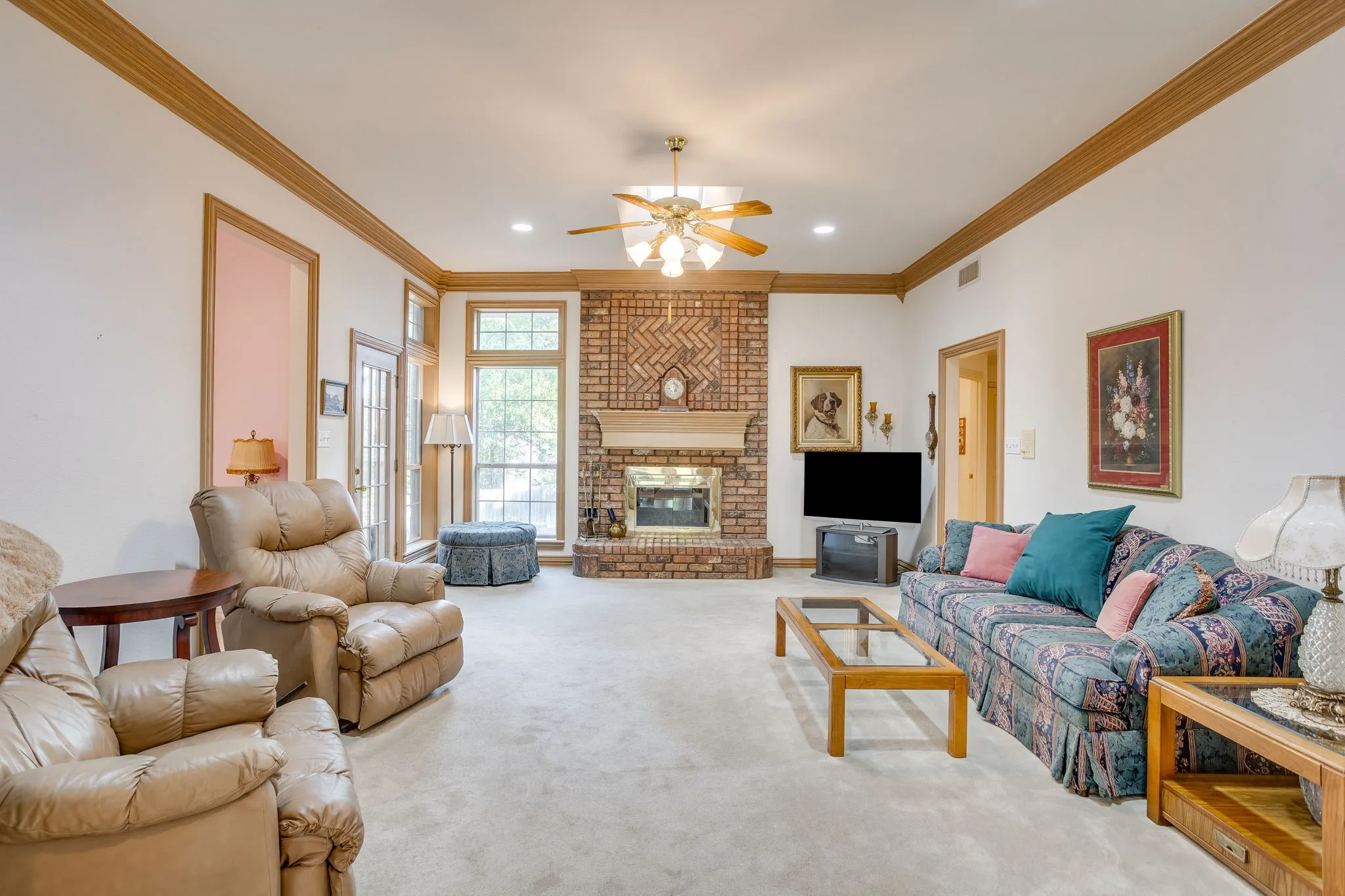 Spacious living area featuring a brick fireplace, tall windows, crown molding, a ceiling fan, and recessed lighting