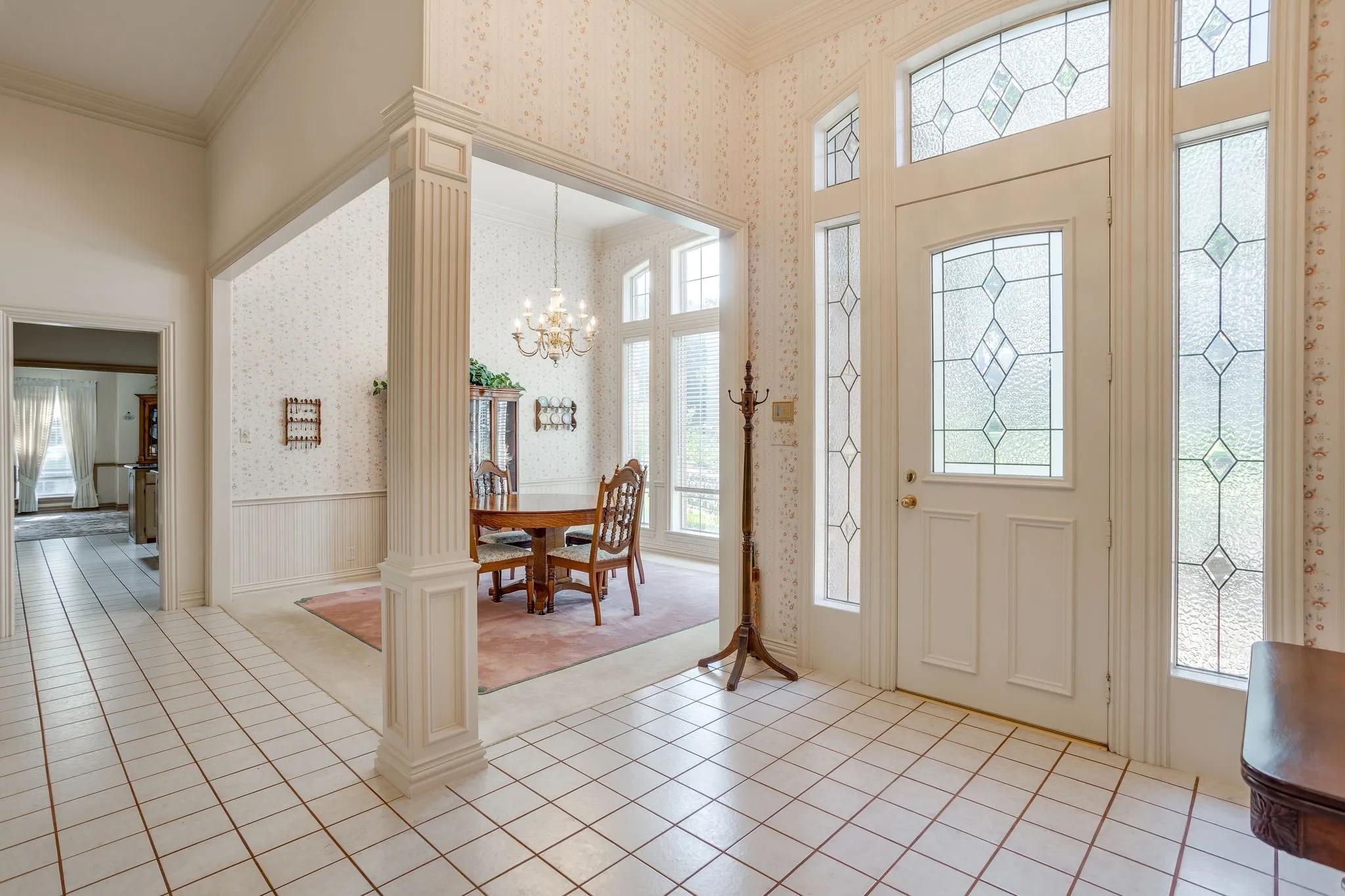 Foyer featuring white tile flooring, a decorative glass entry door with sidelights and transom, and an arched entryway with fluted columns