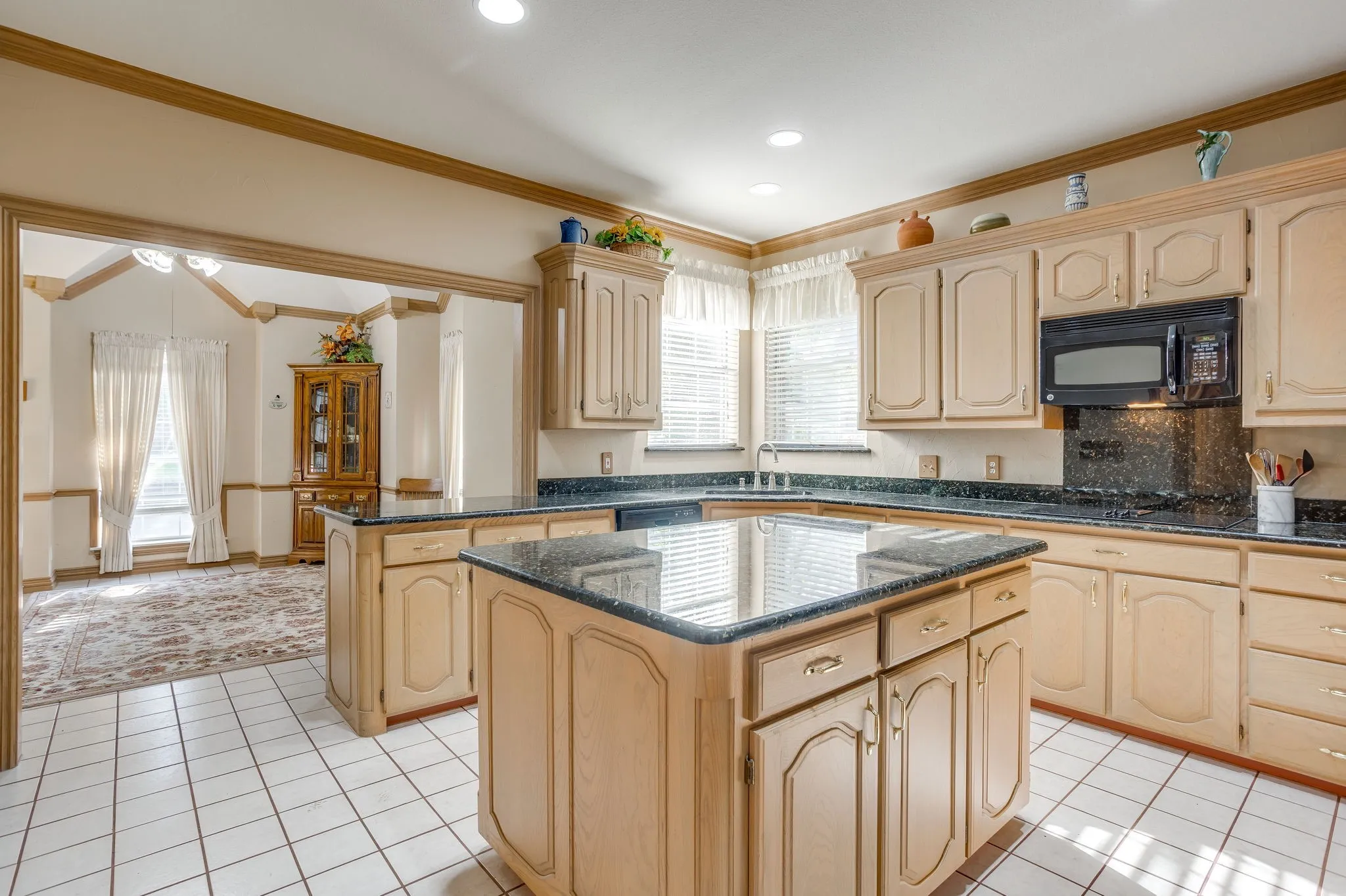 Kitchen featuring two islands with dark countertops, extensive light-toned cabinetry, tile flooring, and integrated appliances