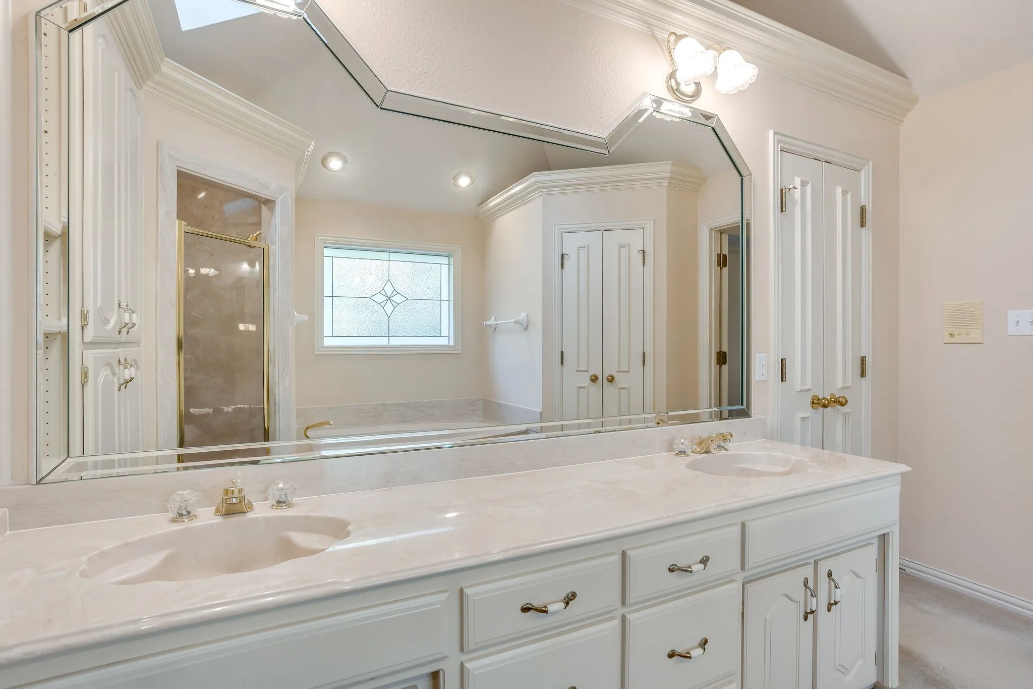 Dual vanity with integrated sinks, white cabinetry, and a large custom-shaped mirror