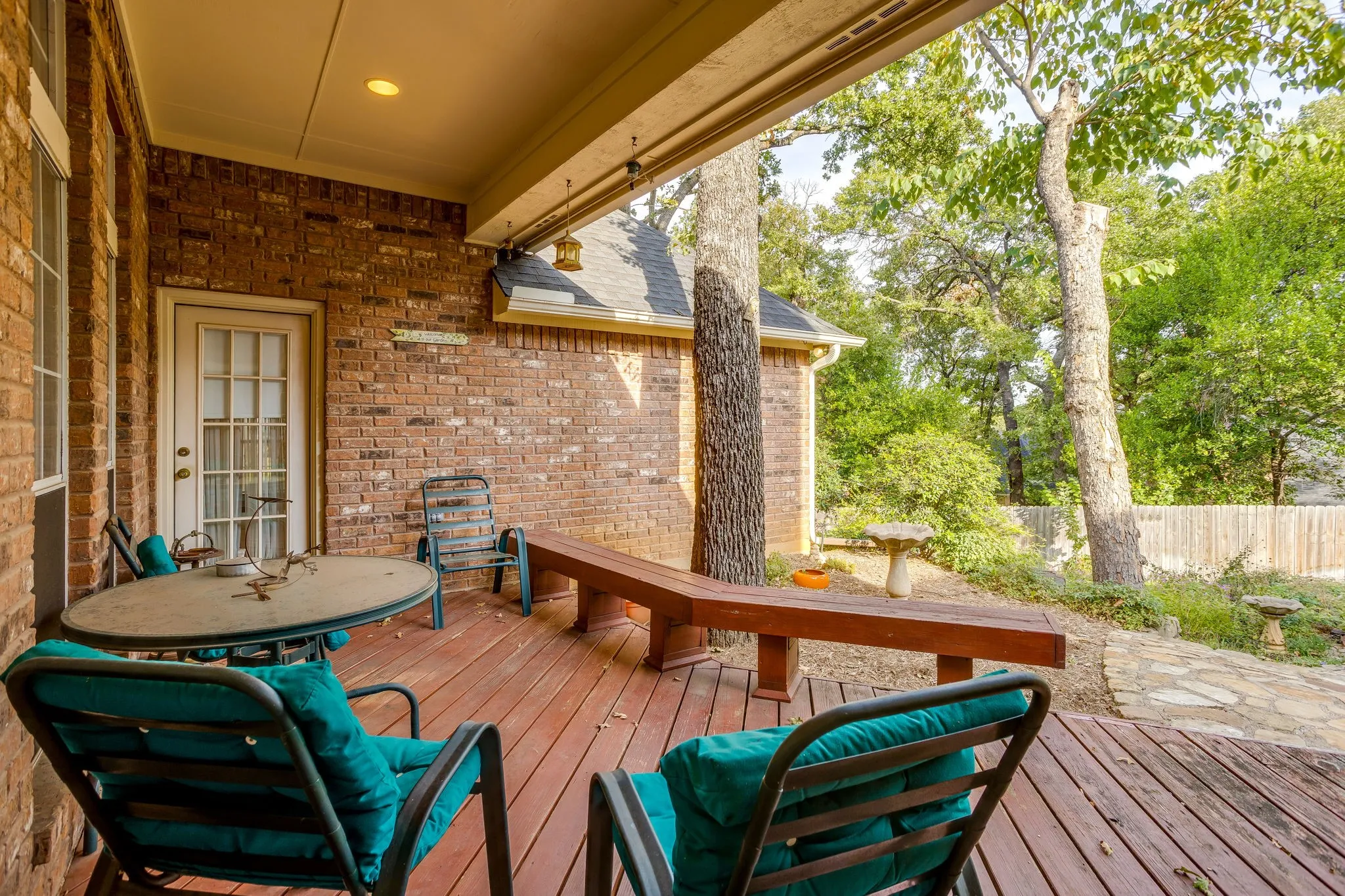 Covered outdoor deck with a red brick exterior, recessed lighting, and a glass-paneled door