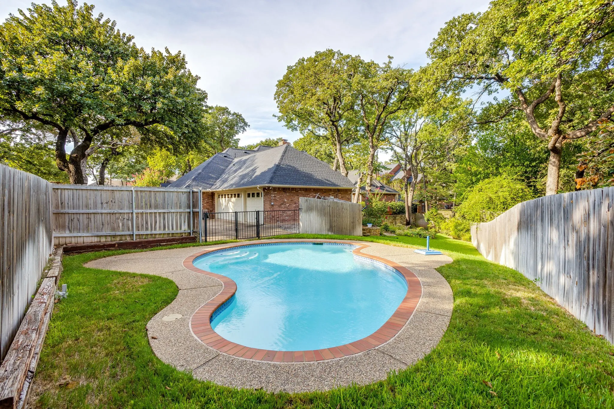 Kidney-shaped swimming pool with brick coping and exposed aggregate decking