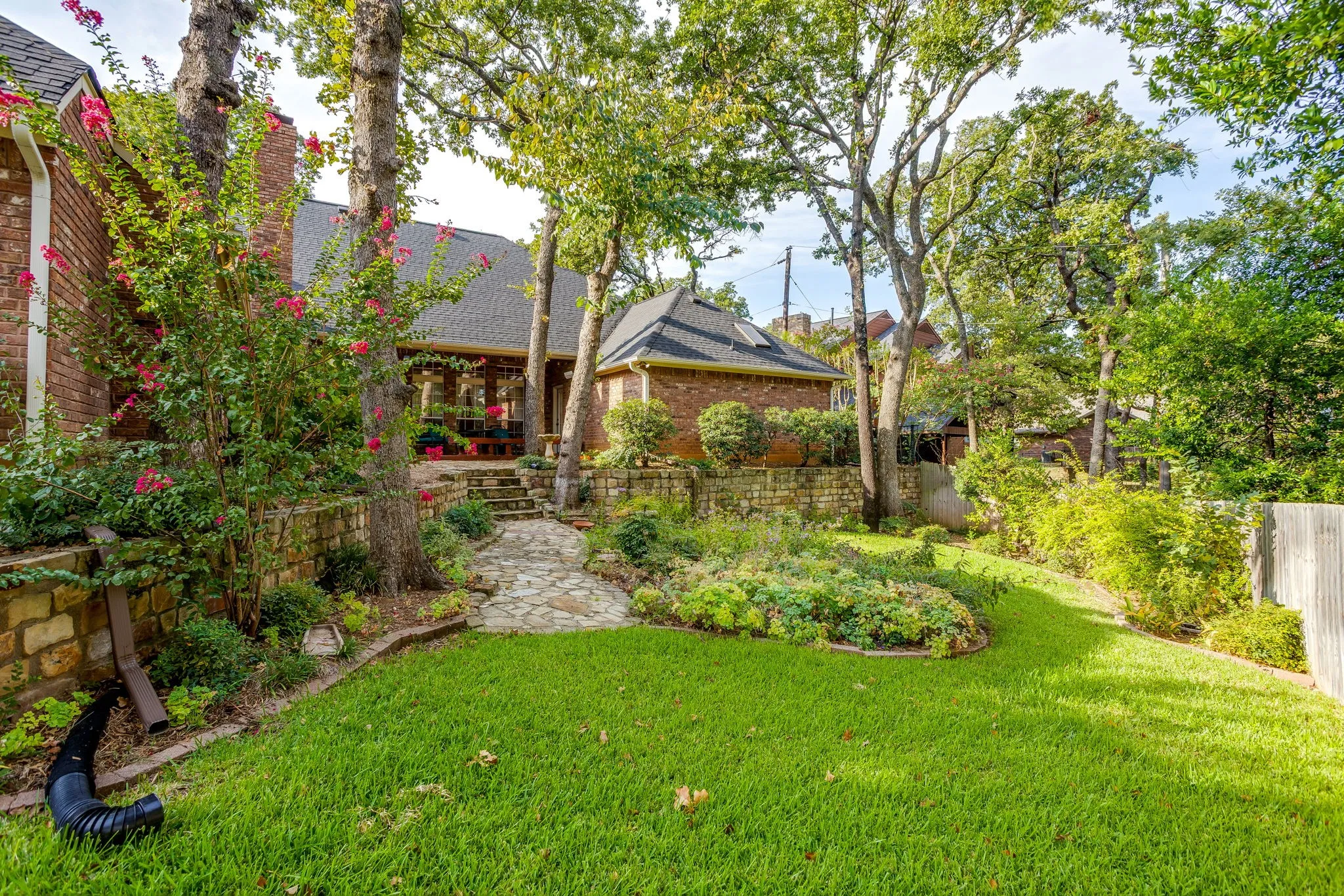 Expansive backyard with a stone-paved pathway, mature trees, and layered landscaping