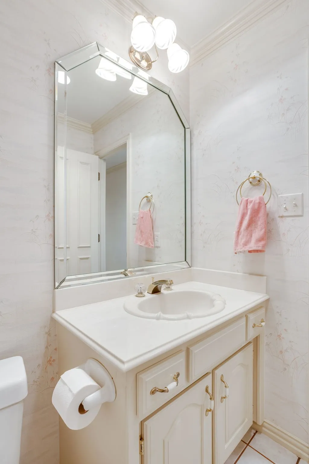 Beveled mirror with an ornate light fixture, vanity with integrated basin, decorative cabinet hardware, and crown molding