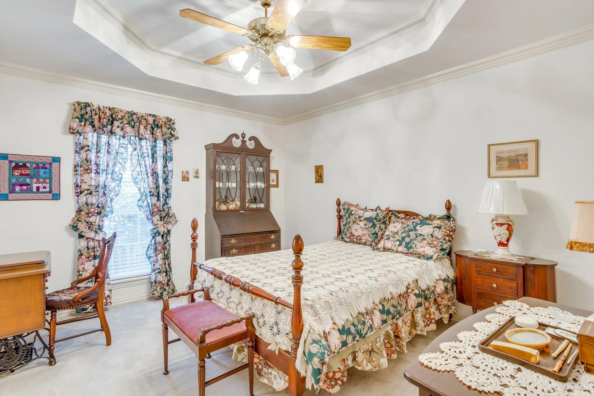 Tray ceiling with crown molding, ceiling fan with integrated lighting, window with blinds, and light-colored carpet