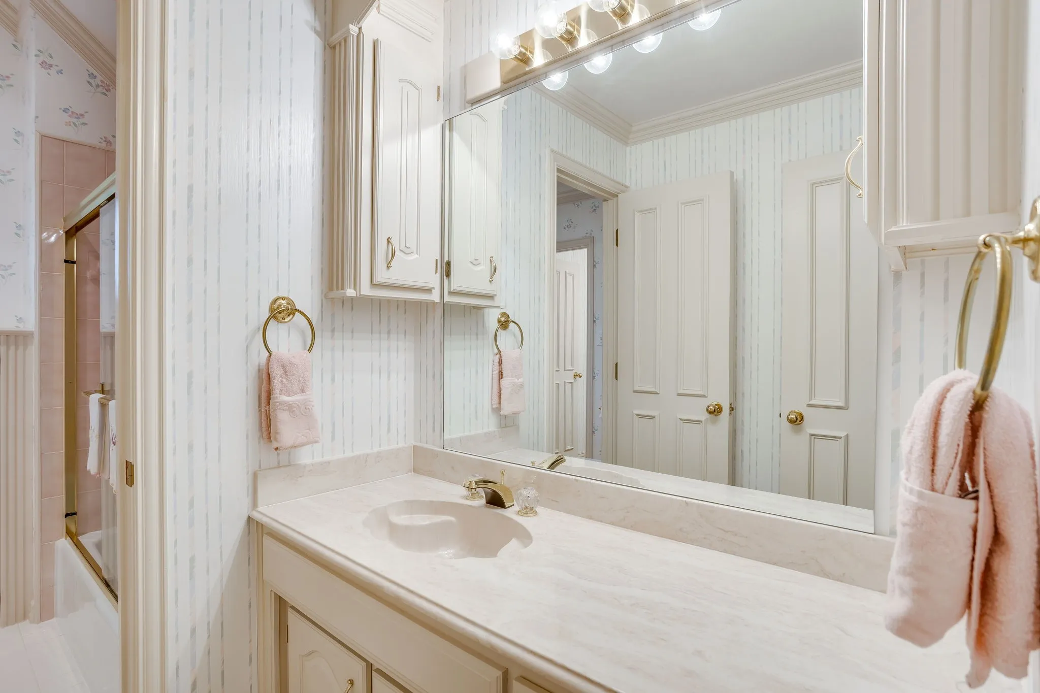 Vanity with an integrated sink, polished brass fixtures, wall-mounted mirror, and built-in cabinetry