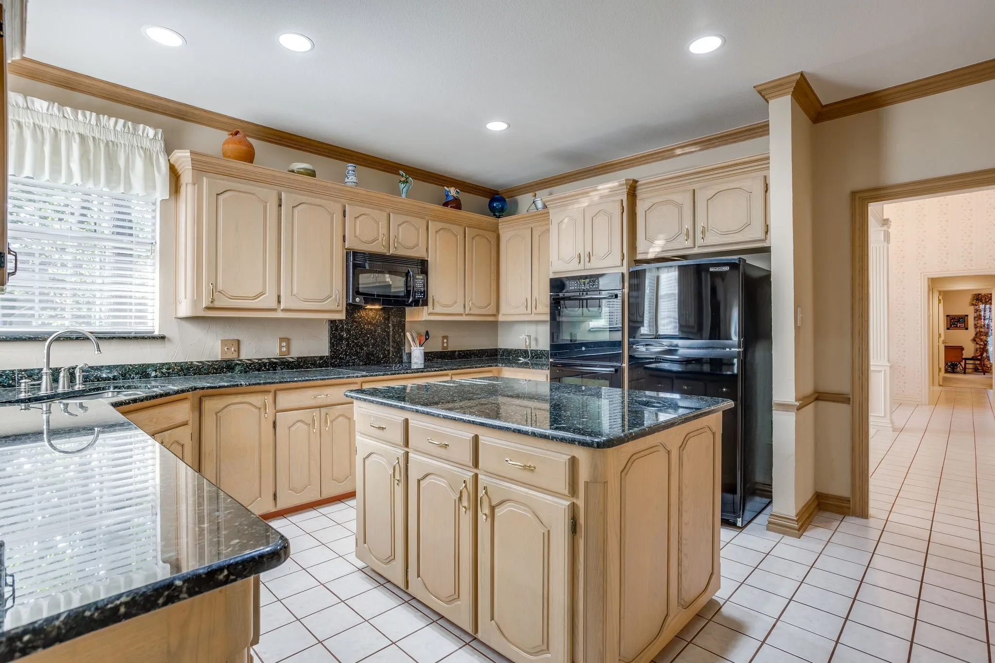 U-shaped kitchen with light wood cabinetry, dark speckled countertops, and a central island