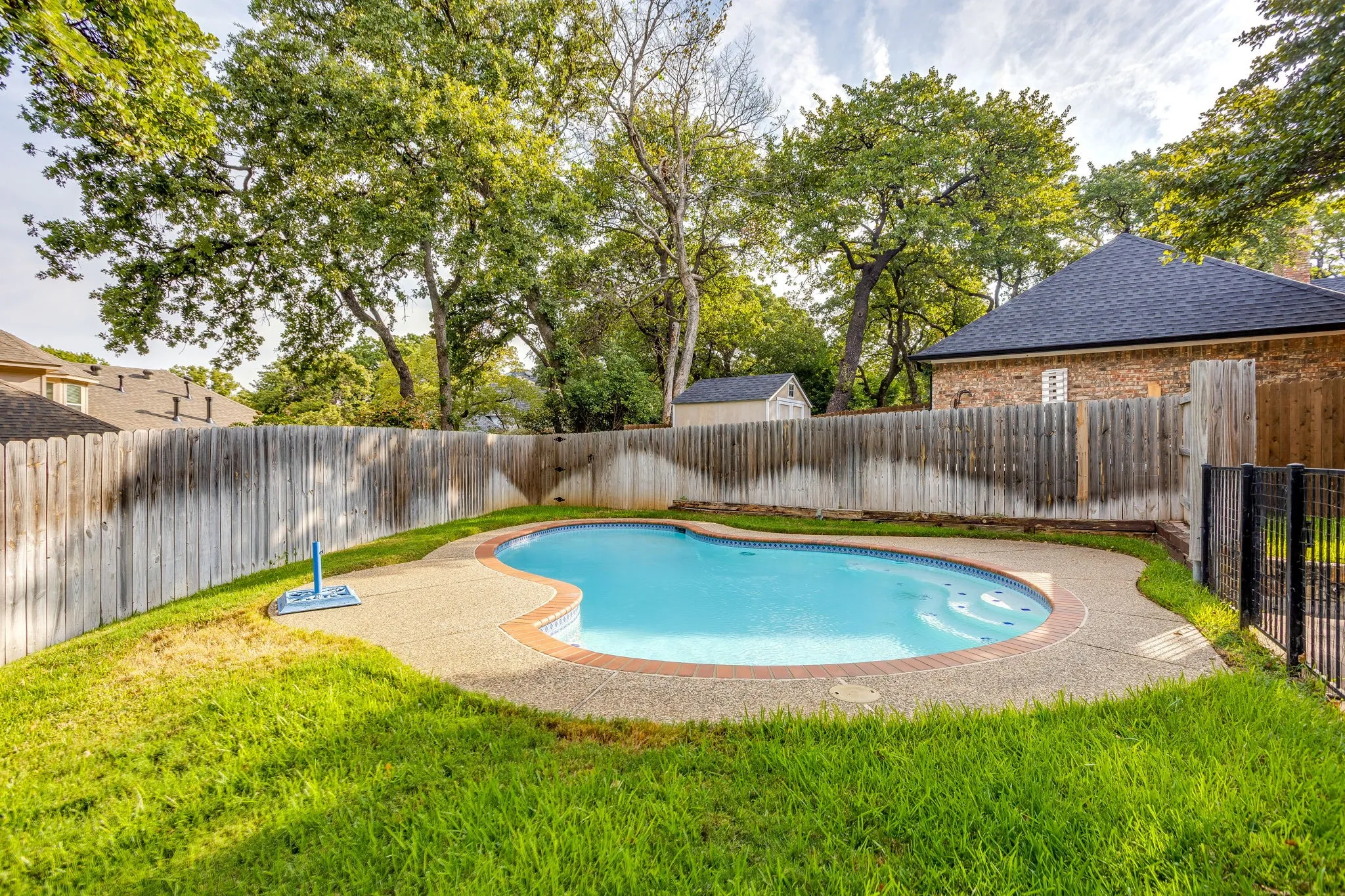 Curved in-ground swimming pool with an exposed aggregate surround and brick coping