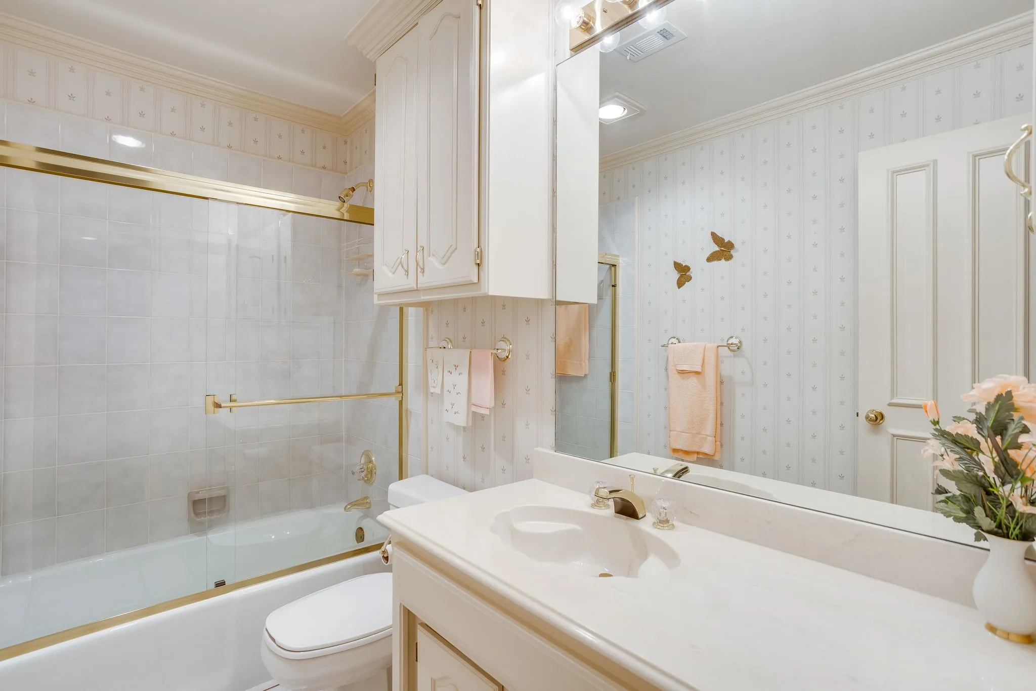 Bathroom featuring a single vanity, integrated sink, gold-tone fixtures, built-in cabinetry, and a tub with a sliding glass​​‌​​​​‌​​‌‌​‌‌​​​‌‌​‌​‌​‌​​​‌​​ enclosure
