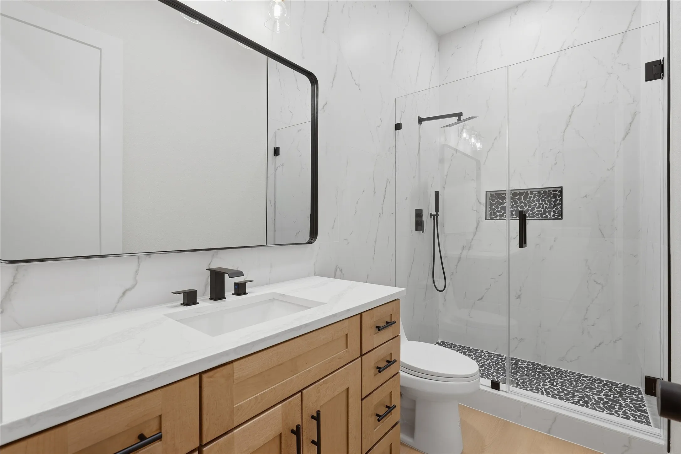 Modern vanity with light wood-finish cabinetry, white countertop, and matte black fixtures