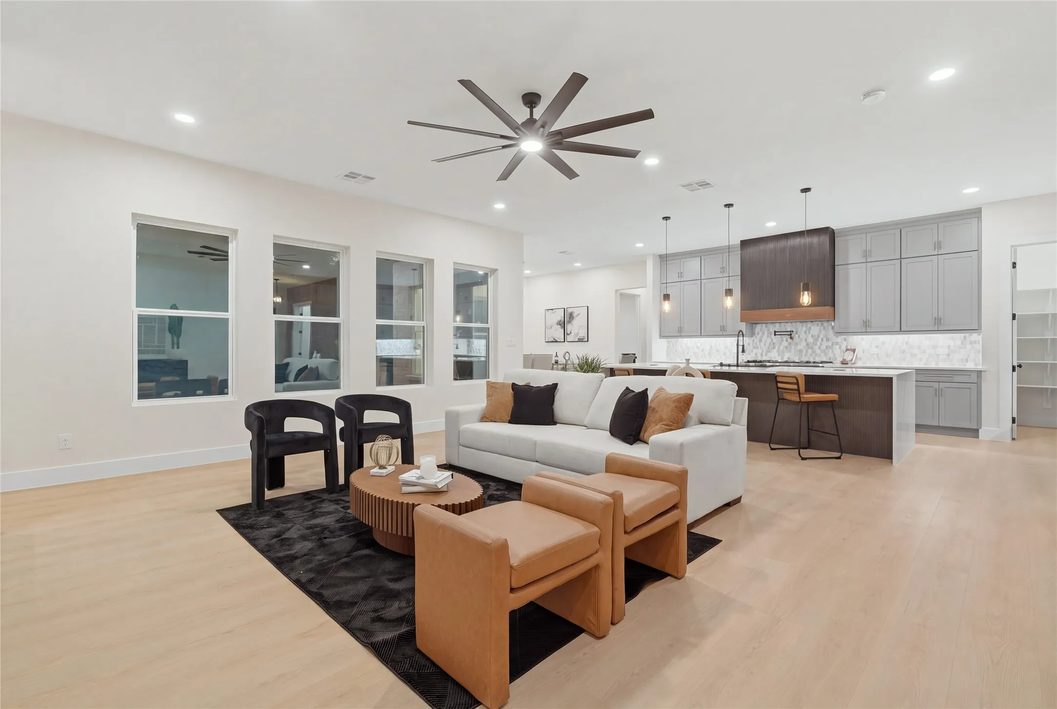 Open-concept living space with light-tone wood-finish flooring, recessed lighting, and a dark-tone ceiling fan