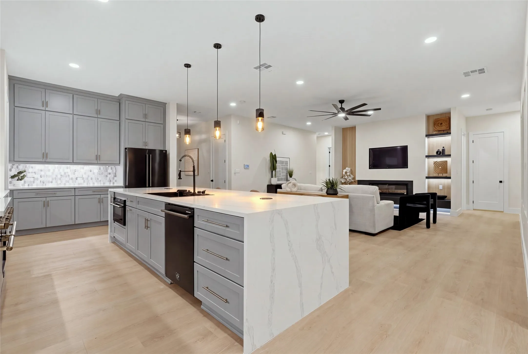 Kitchen featuring a large island with waterfall edge countertop, gray cabinetry, black appliances, and pendant lighting