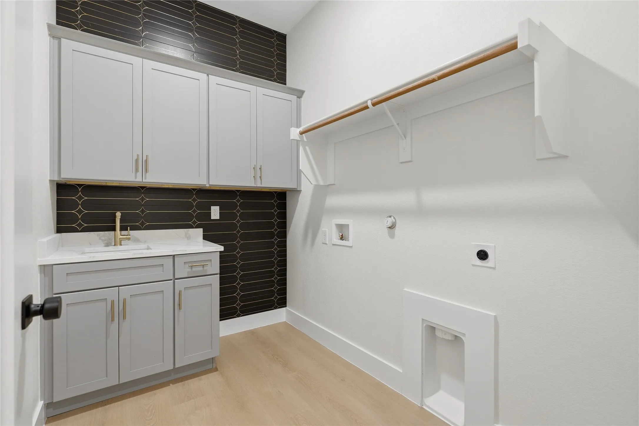 Light wood-finish flooring, built-in cabinetry, sink with a gold-finish faucet, and a wall-mounted clothing rod