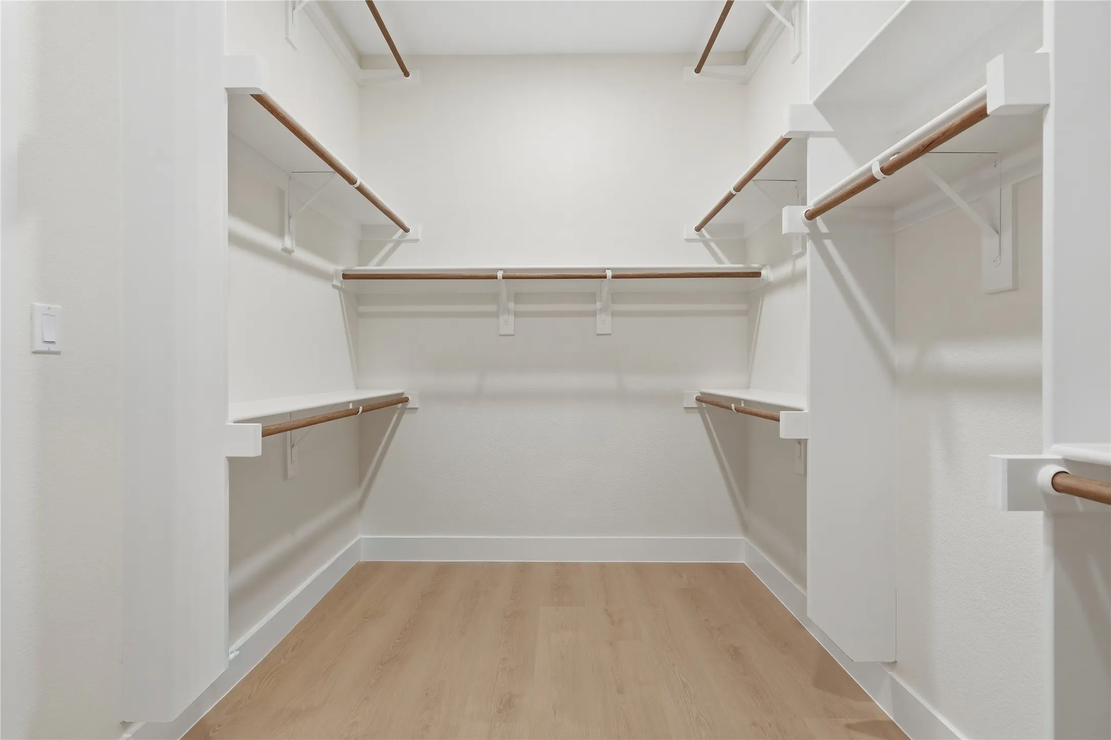 Walk-in closet featuring light wood-finish flooring, white walls, and multiple shelving and hanging rod systems