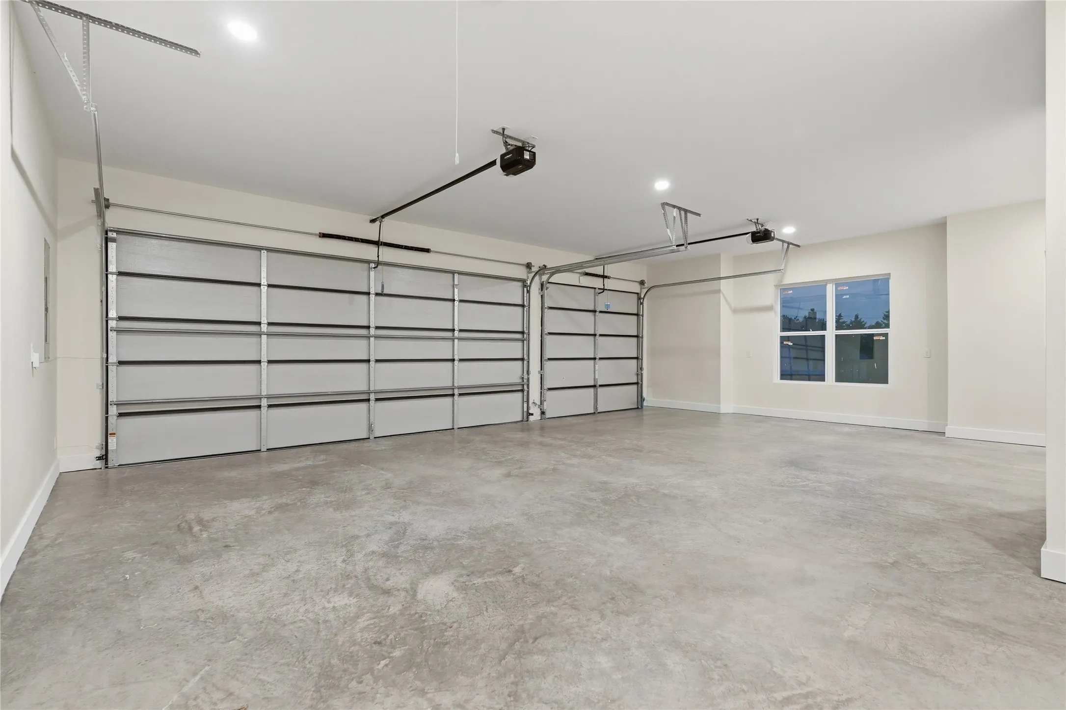 Two-car garage featuring automatic garage door openers, concrete flooring, recessed lighting, and a single window