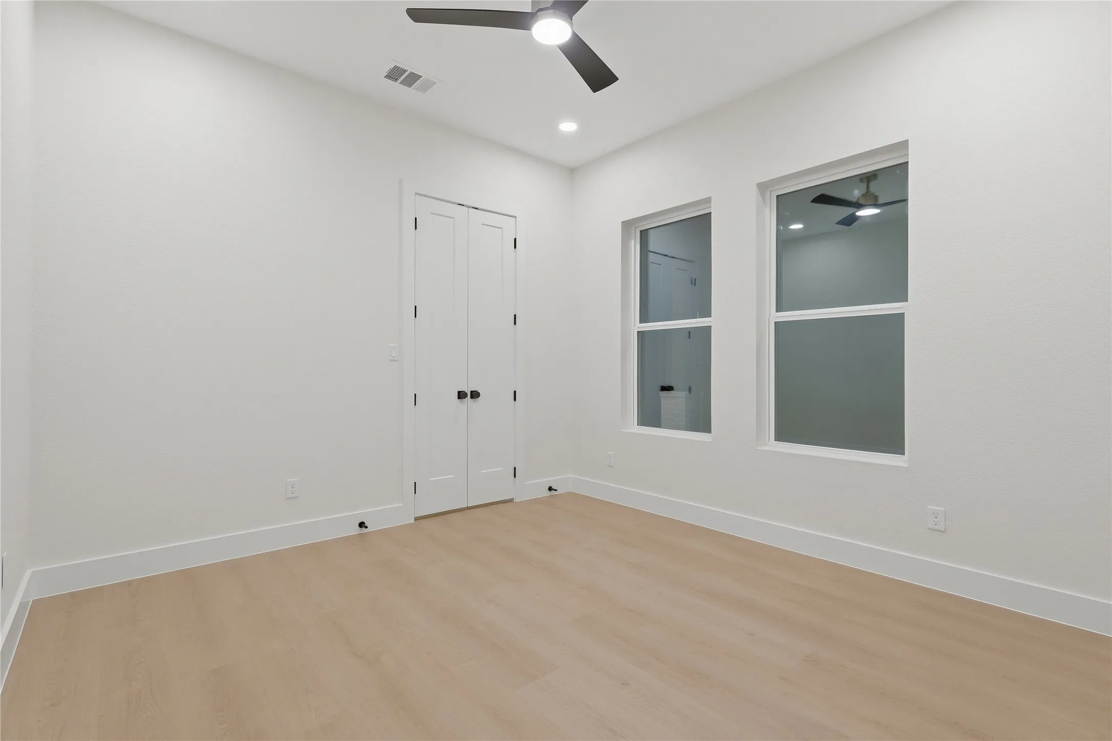 Recessed lighting, wood-finish flooring, two windows, two-panel bifold doors with black hardware, and a ceiling fan