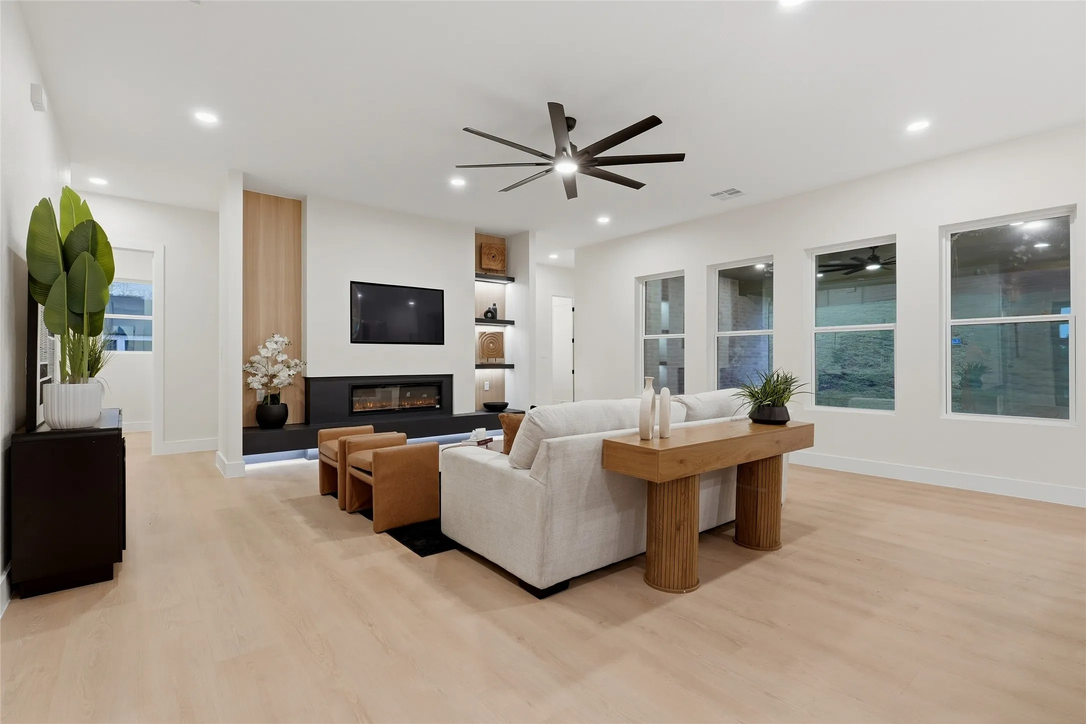 Recessed lighting throughout, wood-finish flooring, a modern electric fireplace, a ceiling fan, and multiple large windows
