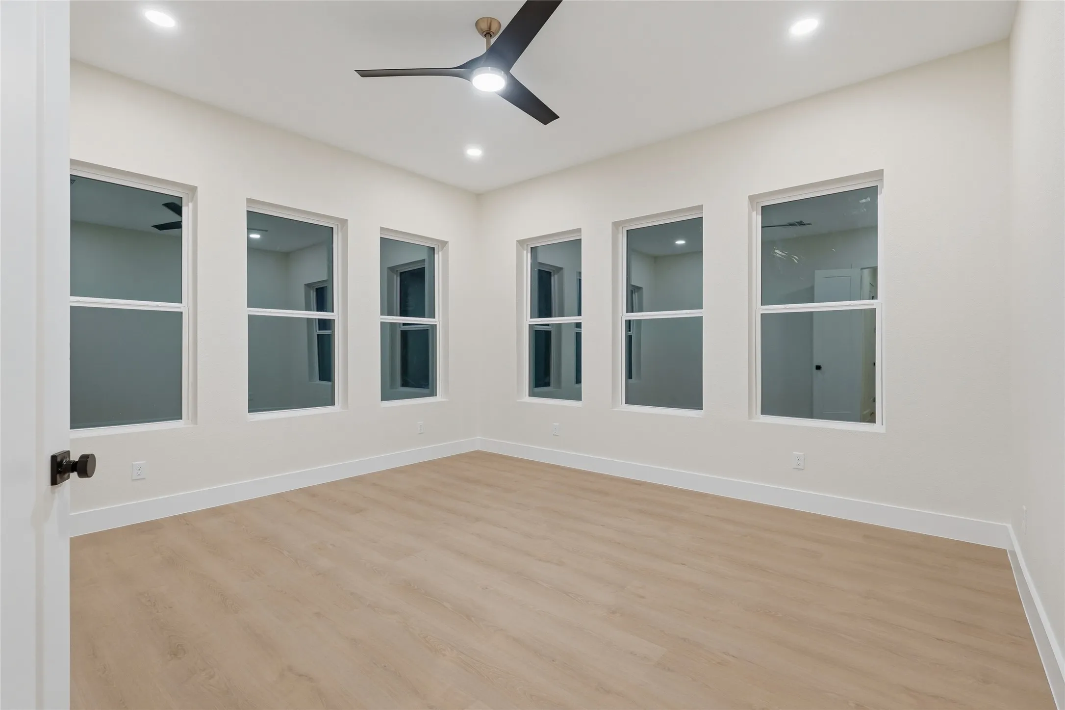 Recessed ceiling lighting, wood-finish flooring, matte black ceiling fan, multiple windows, and white trim throughout
