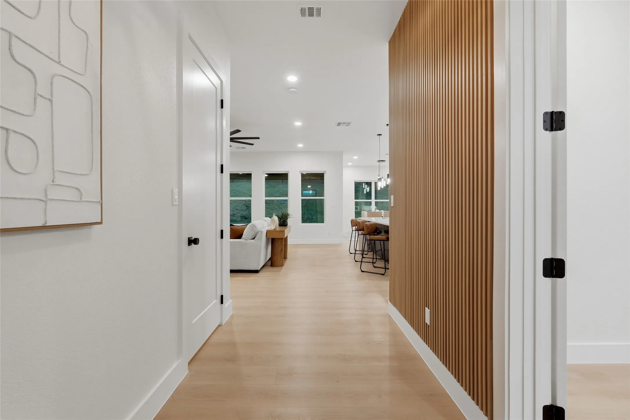 Wide plank wood-finish flooring, recessed lighting, and a slatted wood accent wall