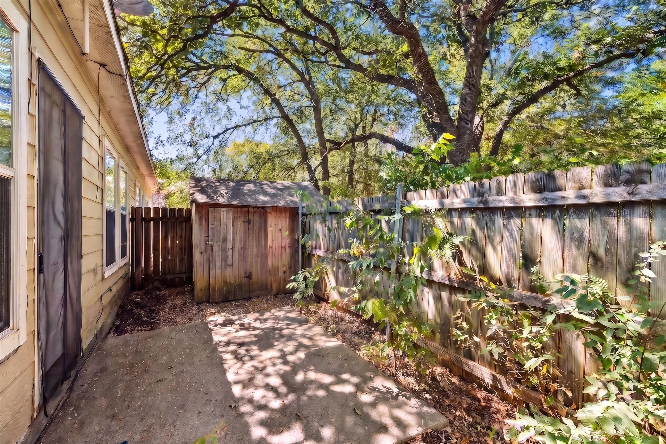 Established tree canopy creates a shaded backyard setting with fenced outdoor space extending beyond the interior living areas. | 5933 Robinwood