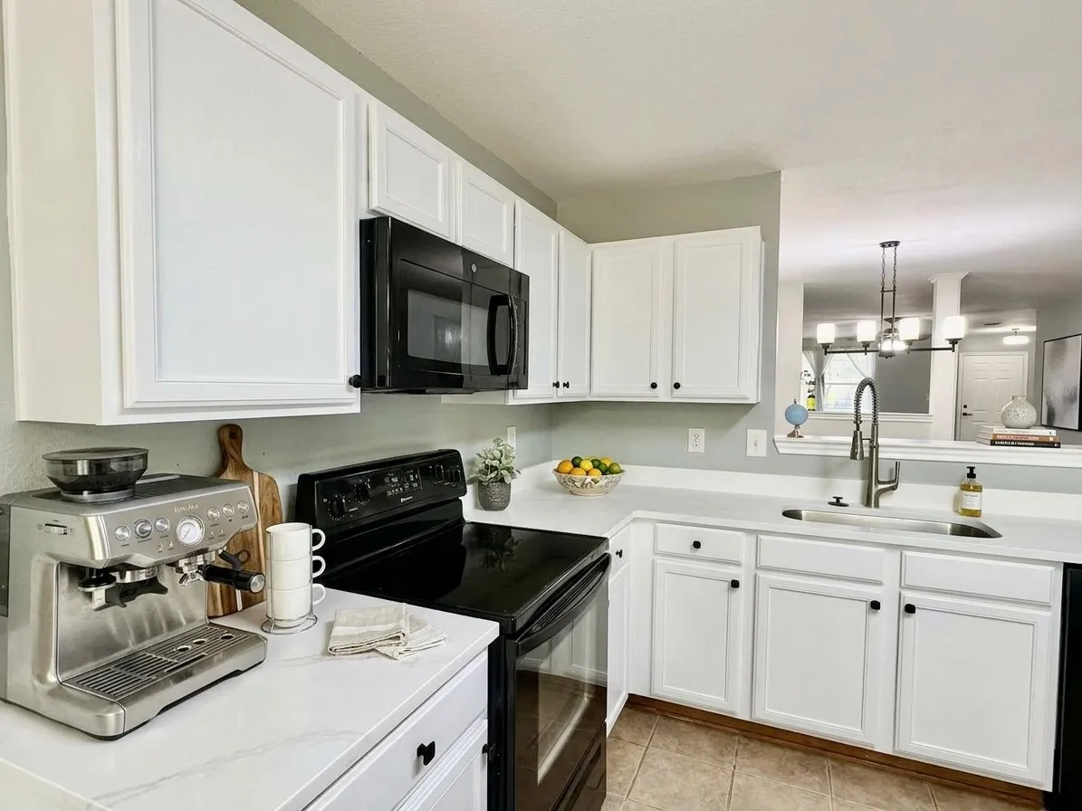 White cabinetry with black hardware, white countertops, built-in microwave, and stainless steel sink with a gooseneck faucet, virtual staged