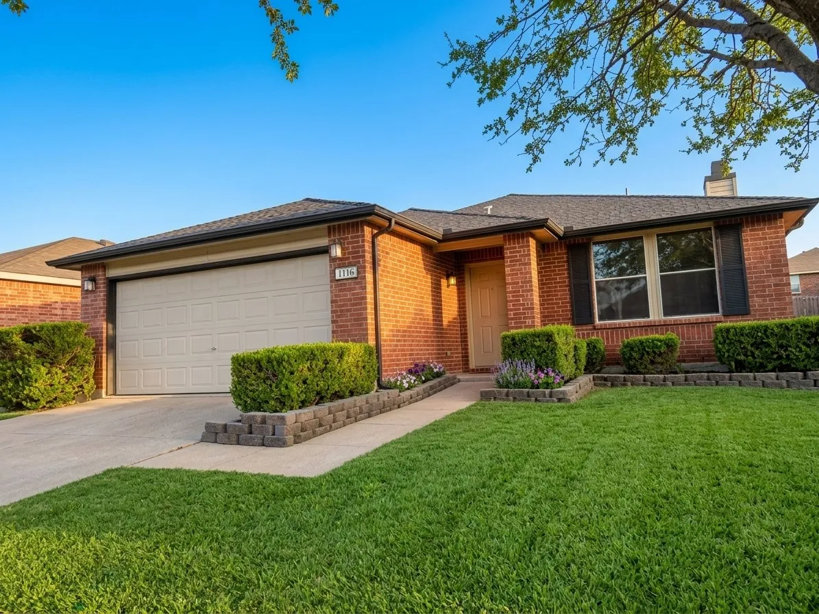 Brick exterior with black shutters and an attached garage, staged grass and trees leaves
