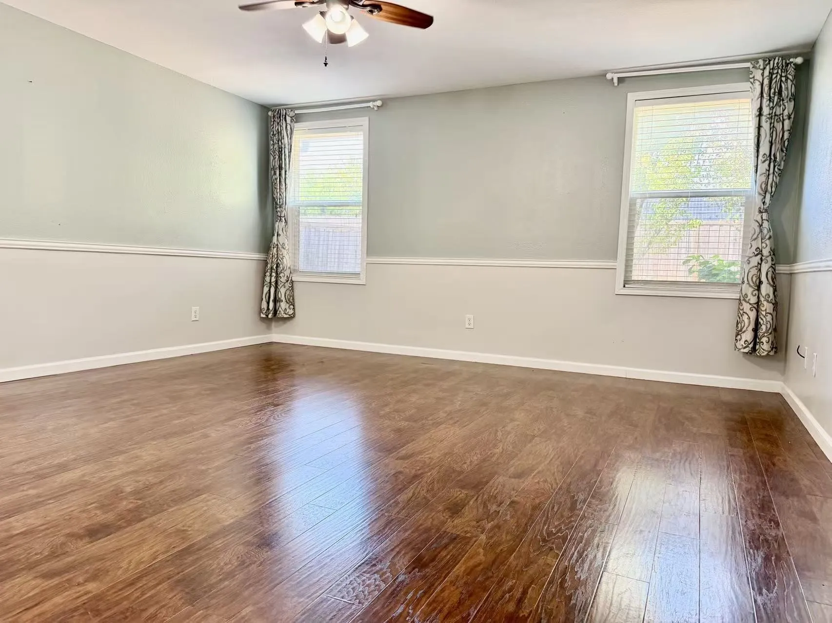 Wood-finish flooring, two windows with blinds, two-toned wall paint, and a ceiling fan with integrated lighting