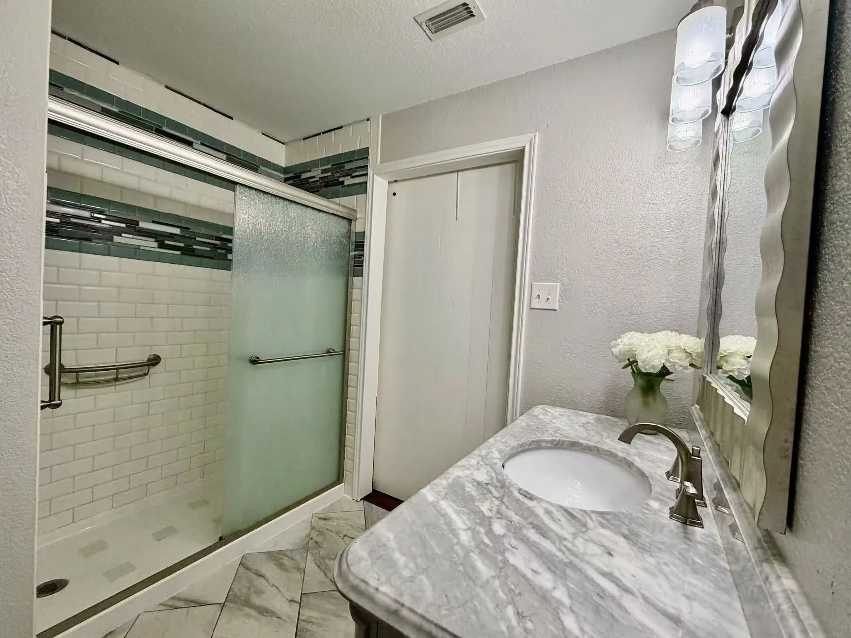 Shower with subway tile surround and decorative accent band, sliding glass enclosure, and grab bar