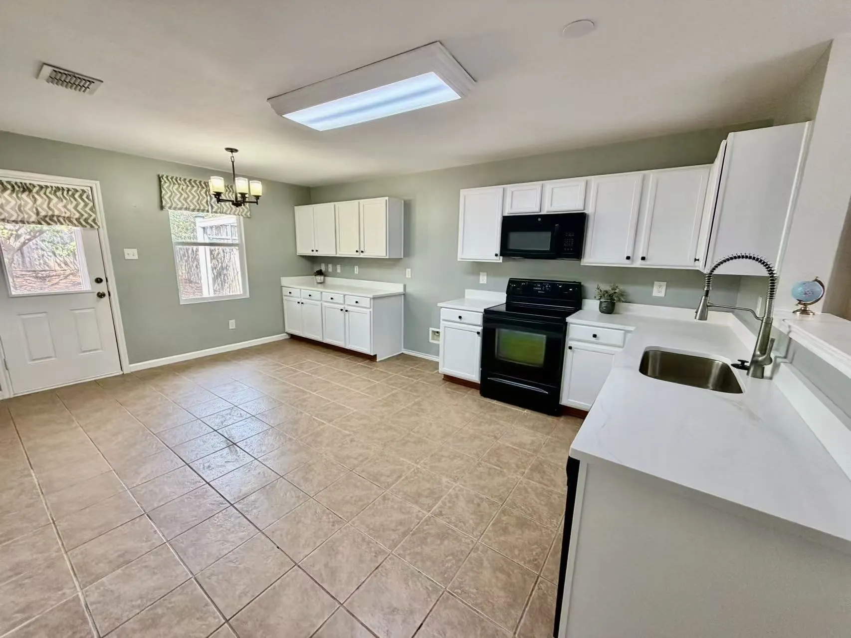 White cabinetry with black hardware, black appliances, light-toned tile flooring, and light-toned countertops