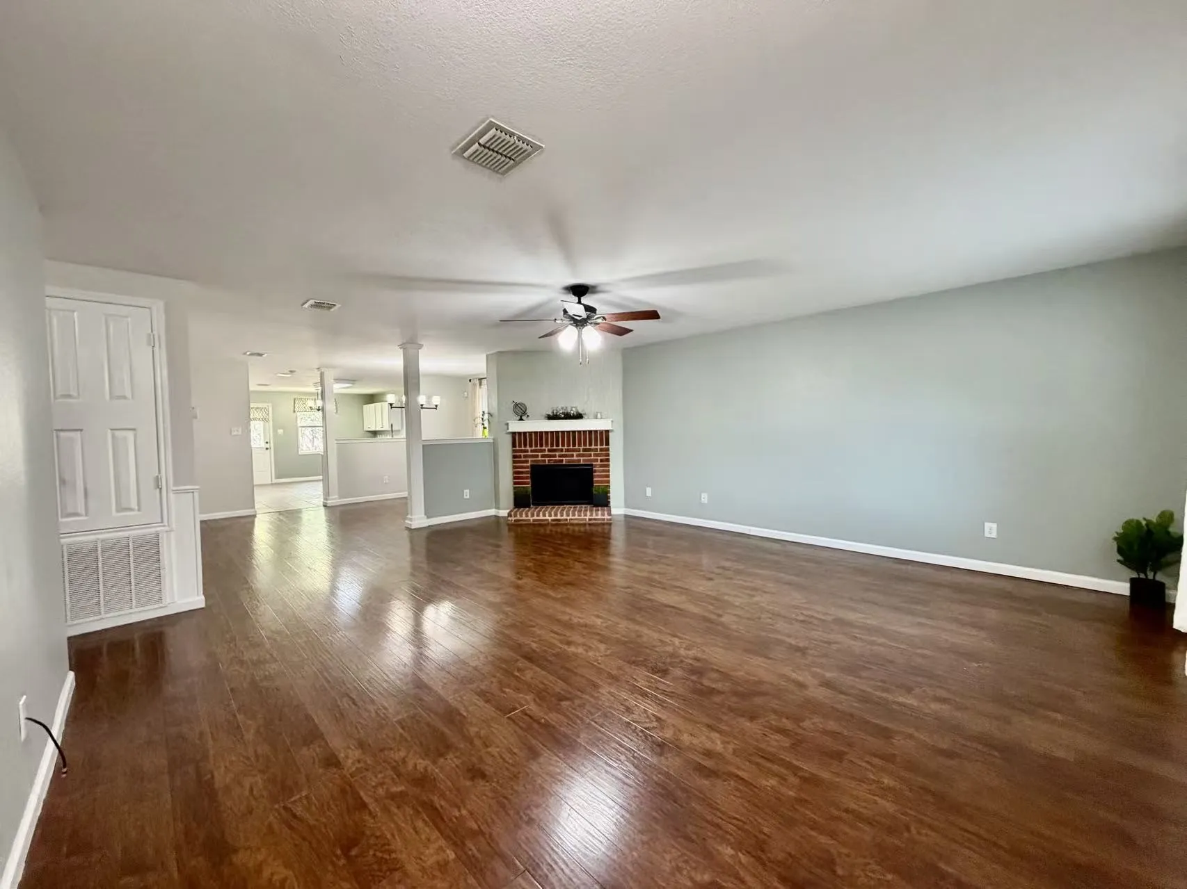 Expansive living area featuring rich wood-finish flooring, a brick fireplace with a mantle, and a ceiling fan