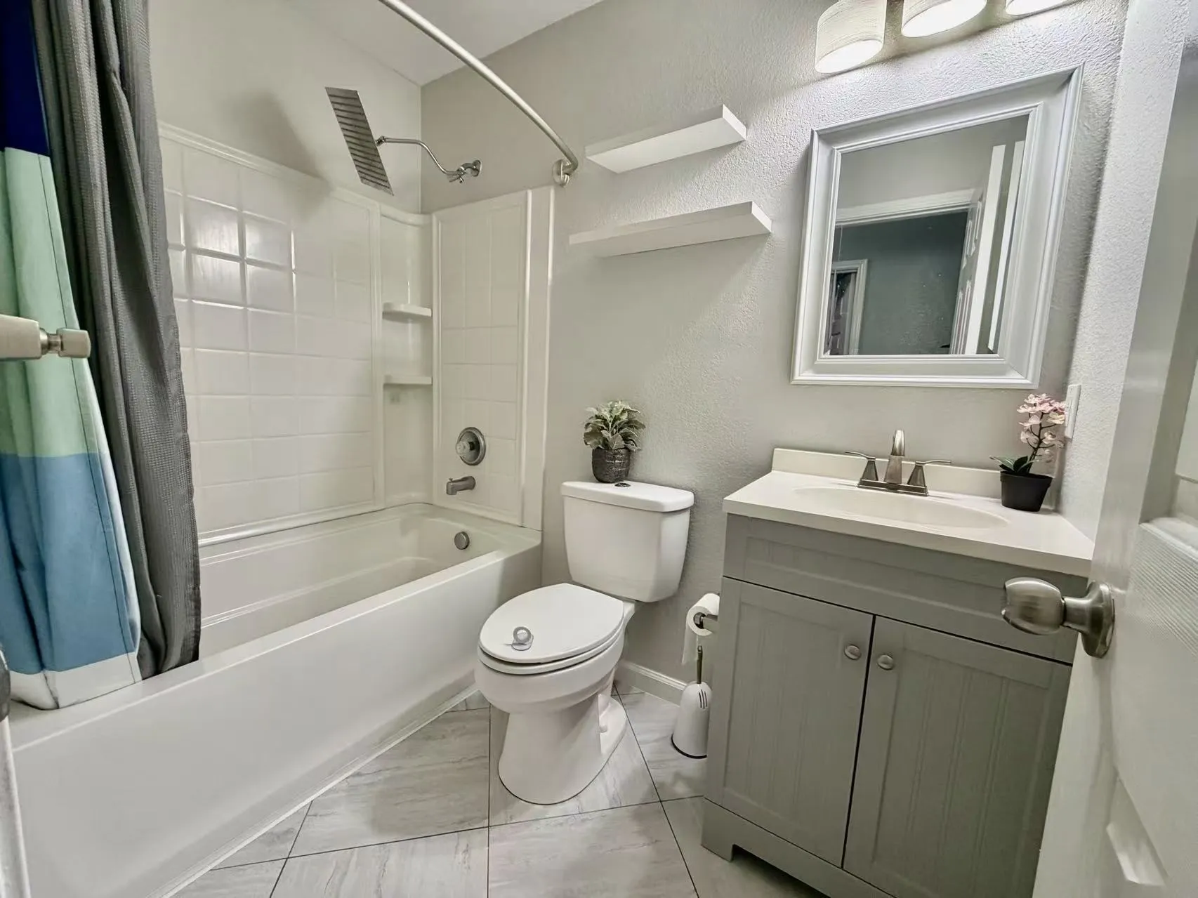 Bathroom featuring a white bathtub, tiled shower surround, light-colored vanity with an integrated sink, and a framed mirror