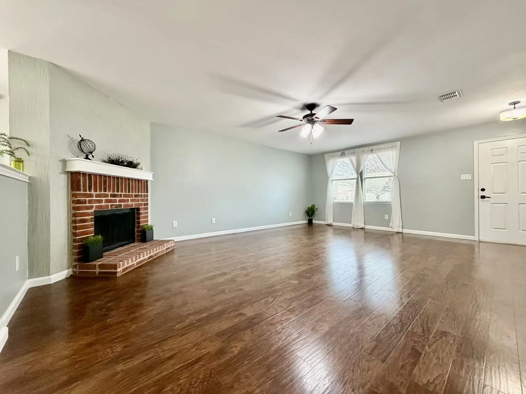 Red brick fireplace with hearth, wood-finish flooring, vaulted ceiling, dual windows, and a ceiling fan