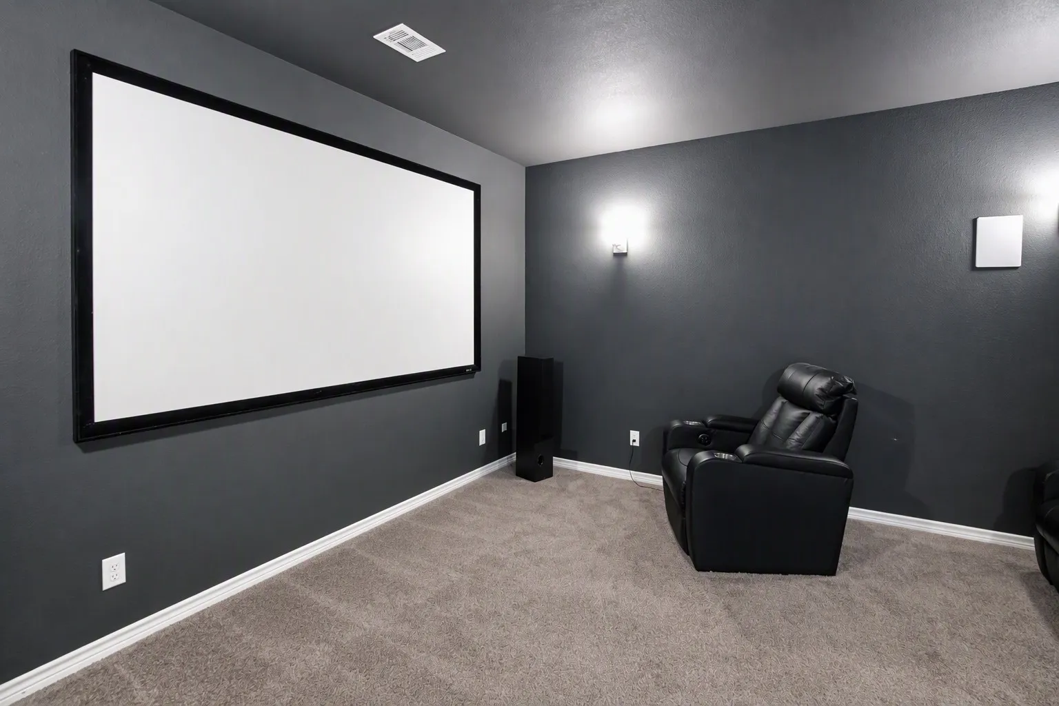 Dedicated media room featuring a large projection screen, dark painted walls, and wall-mounted sconces