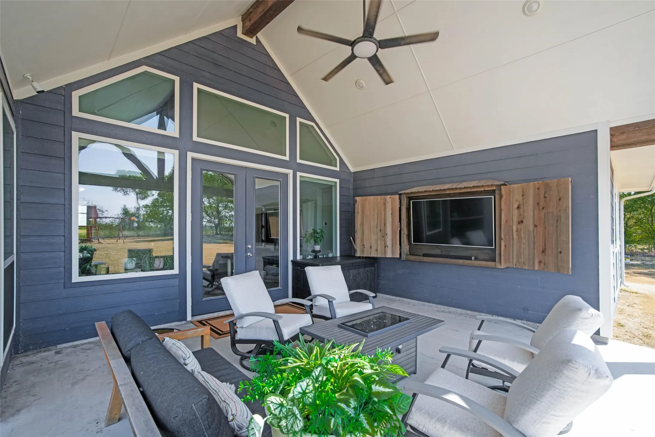 Covered outdoor living space featuring vaulted ceiling, exposed beam, ceiling fan, built-in media cabinet, and large glass panel windows