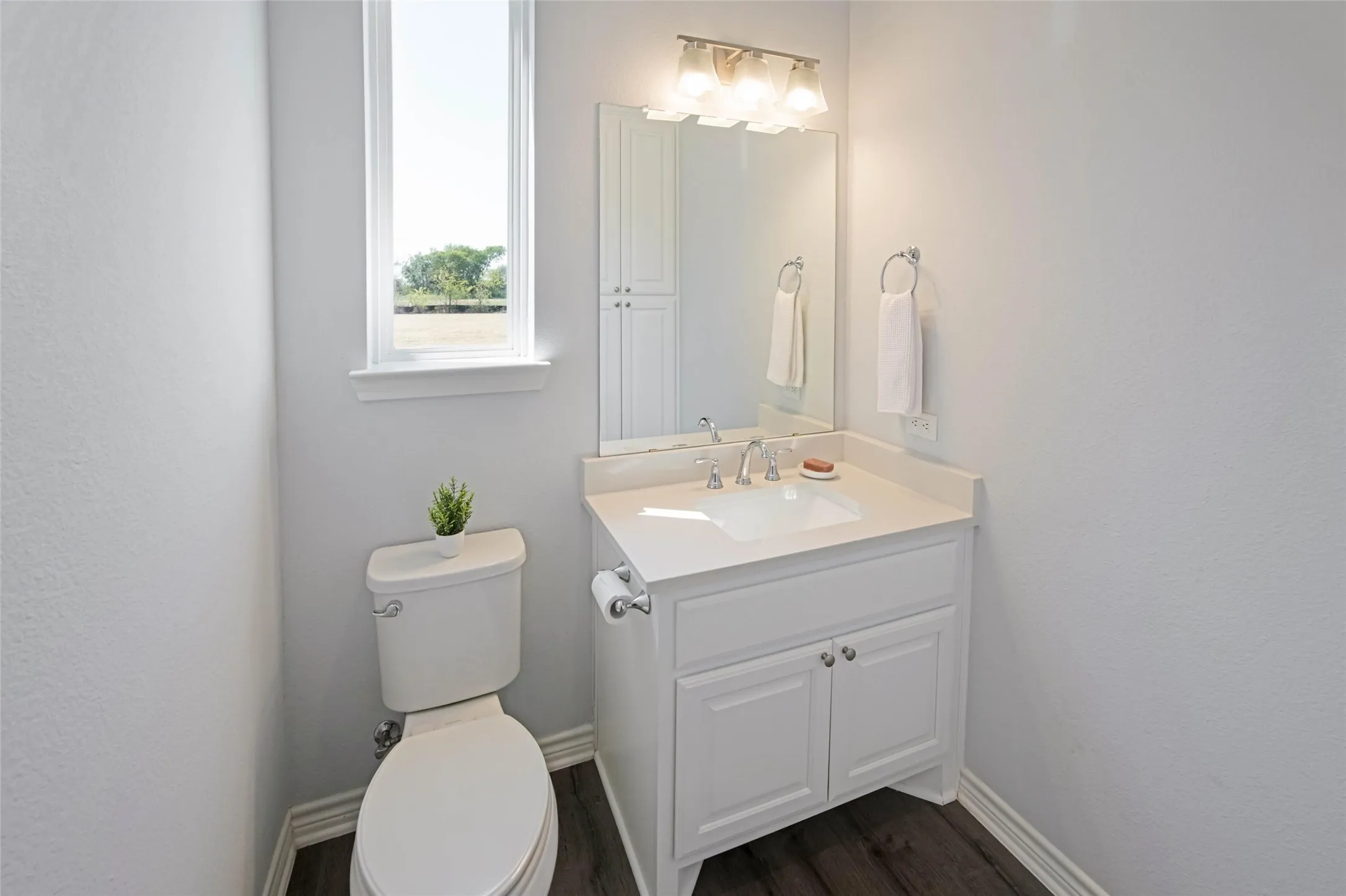 Bathroom featuring a white vanity with a built-in sink, wall-mounted mirror, and dark wood-finish flooring