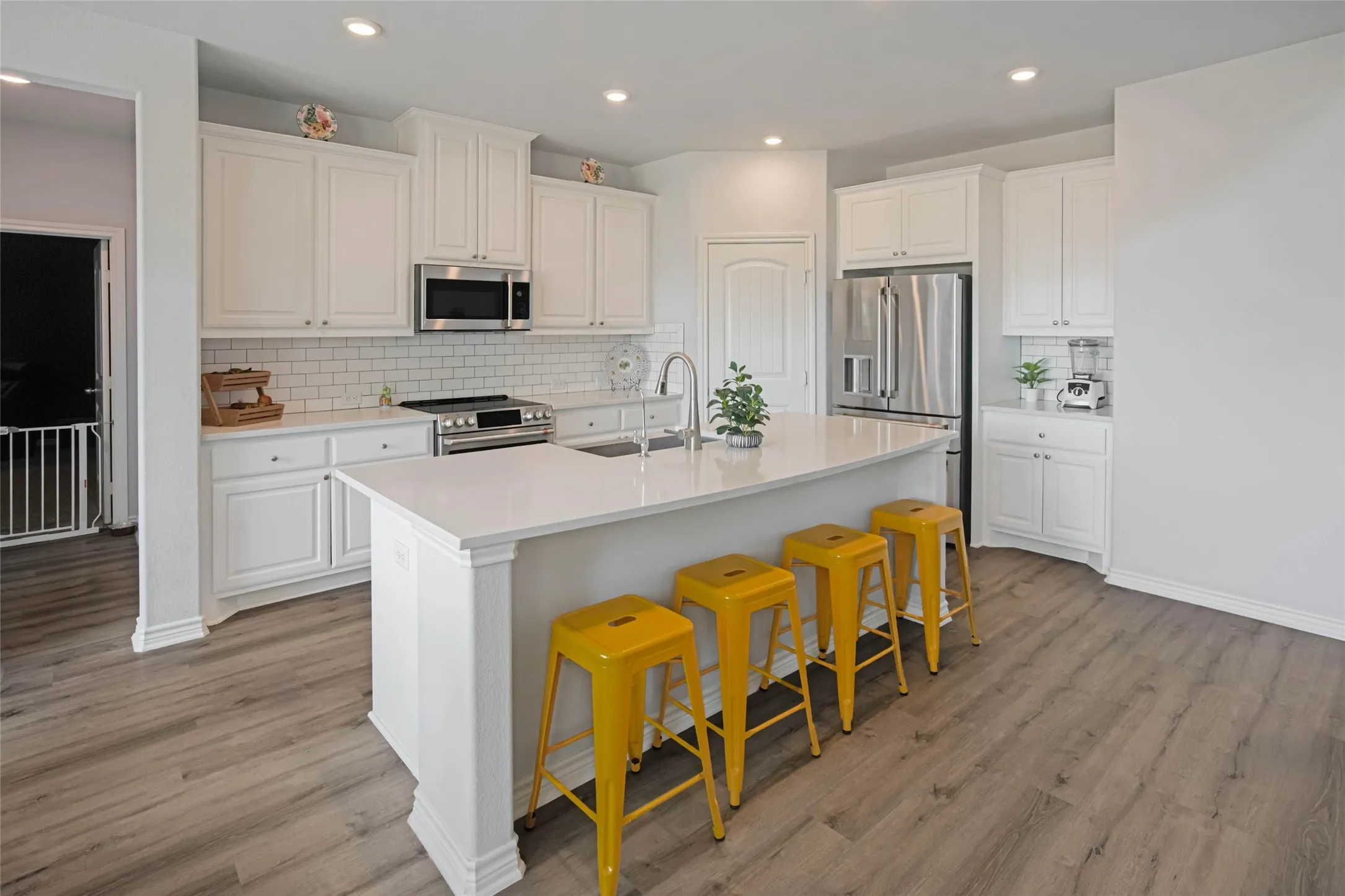 Kitchen featuring white cabinetry, stainless steel appliances, a subway tile backsplash, a large center island with a sink, and wood-finish flooring