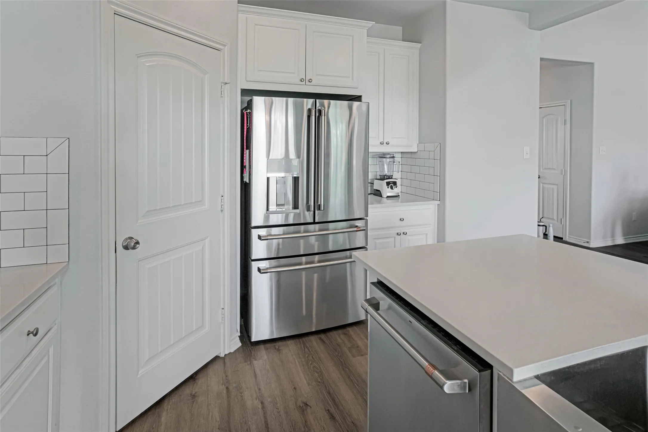 Stainless steel refrigerator, white shaker cabinetry, subway tile backsplash, light-toned countertop, and wood-finish flooring