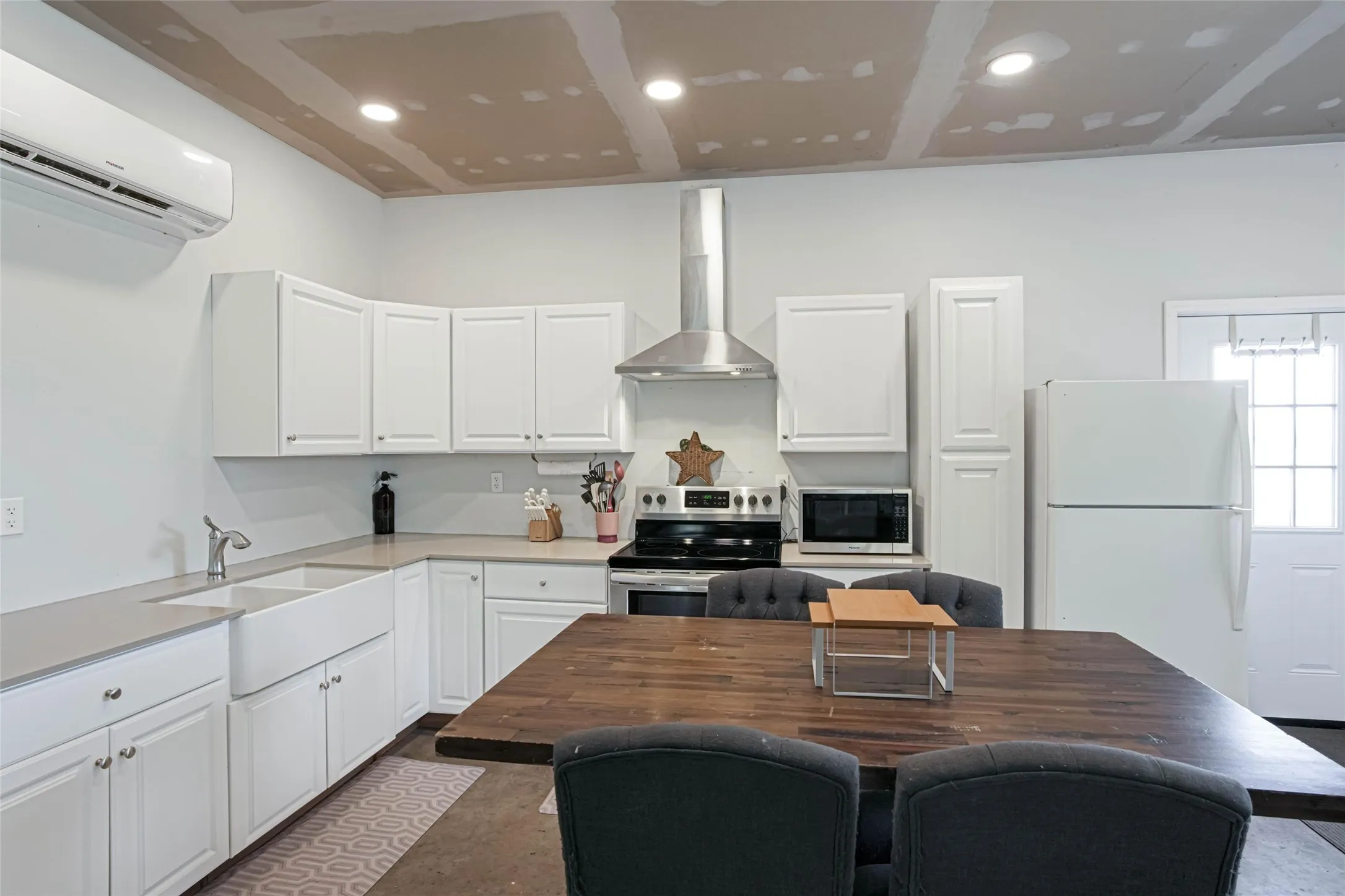 White cabinetry, stainless steel range hood, farmhouse-style sink, white refrigerator, and recessed lighting