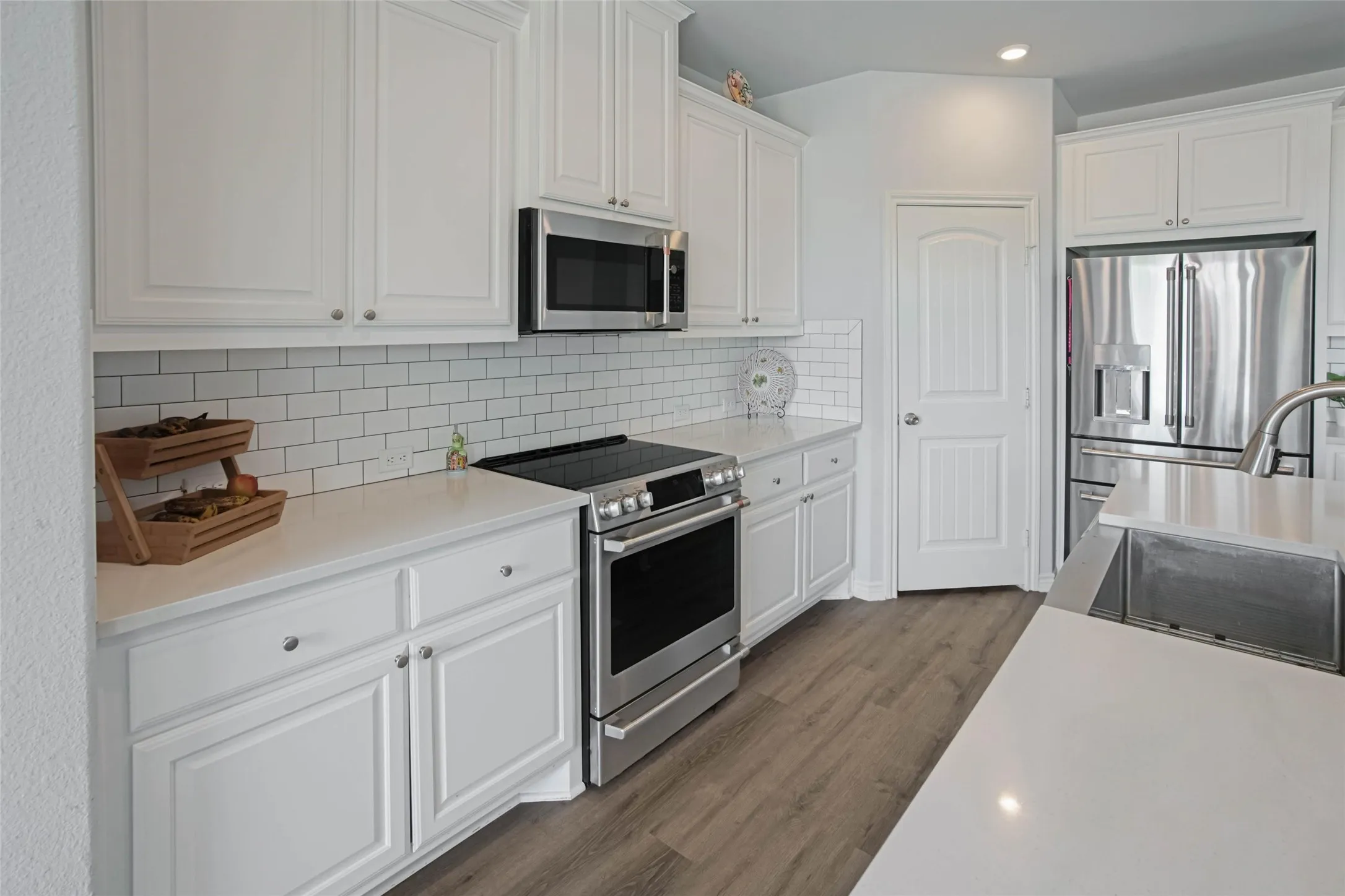 Modern kitchen featuring white shaker cabinetry, stainless steel appliances, a subway tile backsplash, light-toned countertops, and wood-finish flooring