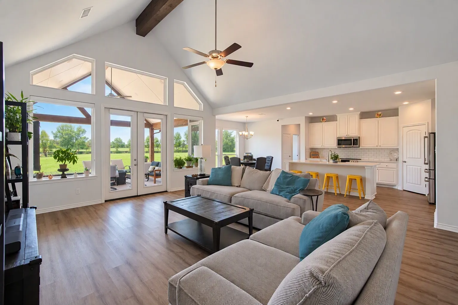 Vaulted ceiling with exposed wood beam, wood-finish flooring, French doors leading to a covered patio, white kitchen cabinetry, and recessed lighting